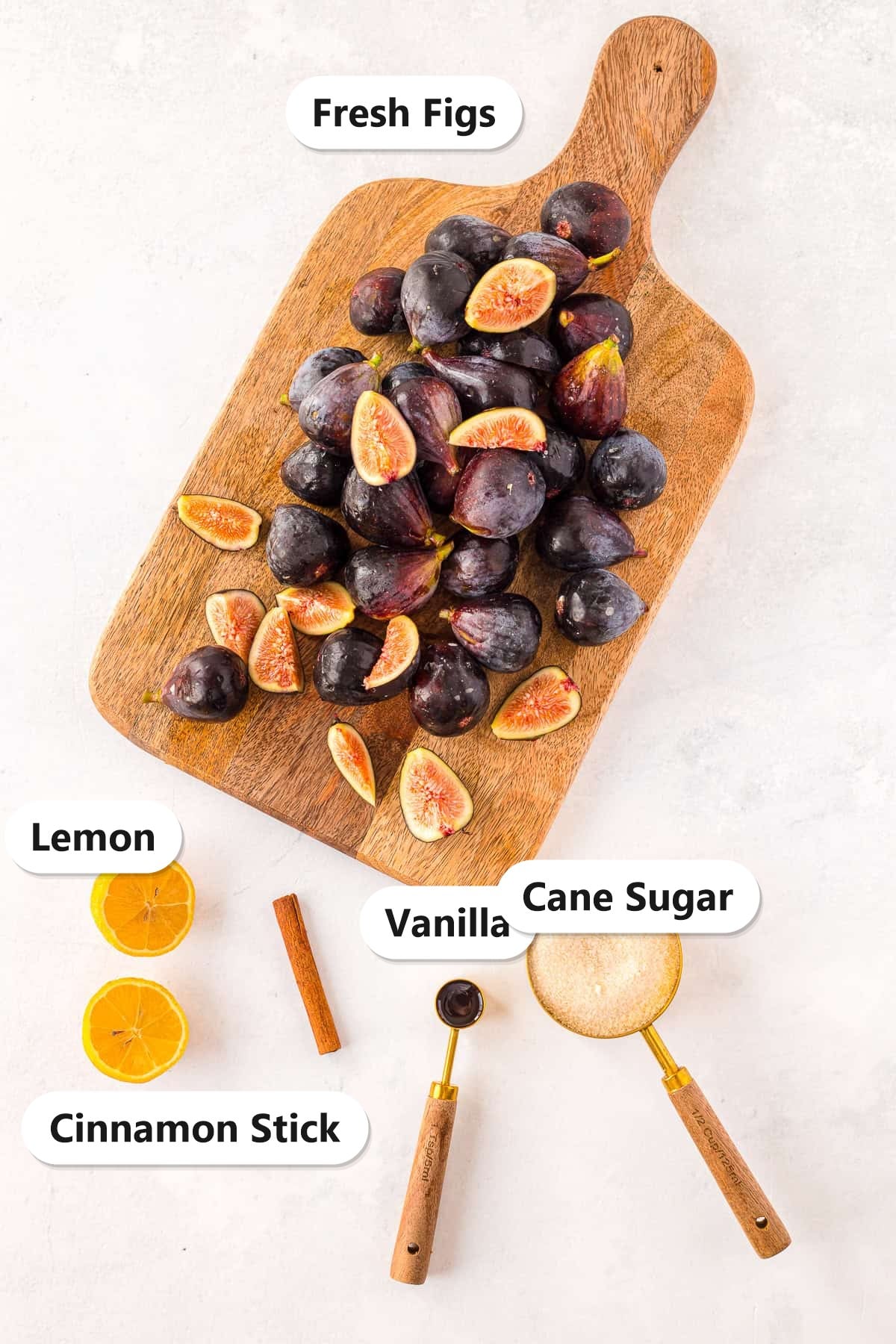 Ingredients for fig jam including fresh figs, lemon, cinnamon stick, cane sugar, and vanilla.