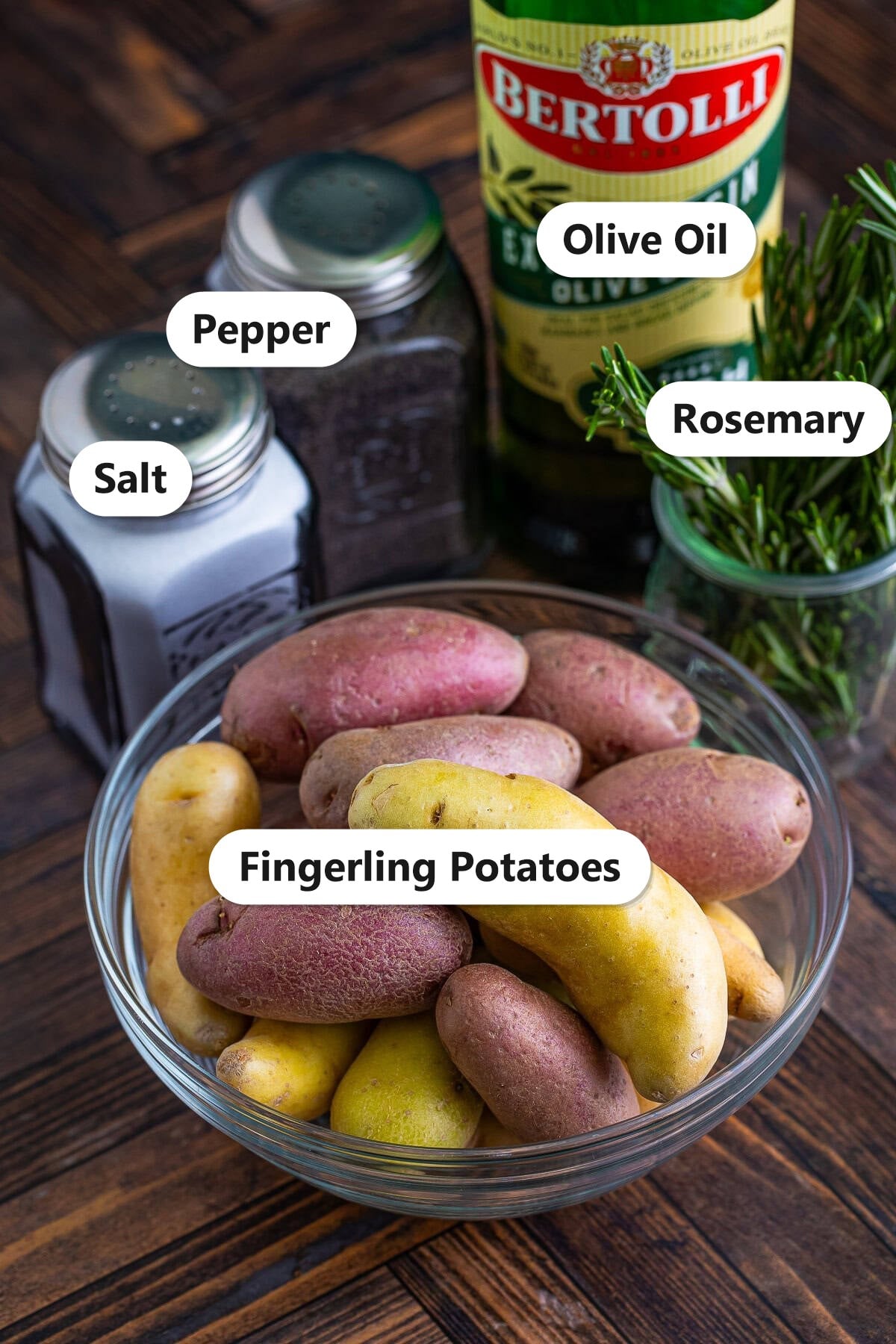 Labeled ingredients to make roasted fingerling potatoes including fingerling potatoes, olive oil, salt, pepper, and rosemary.