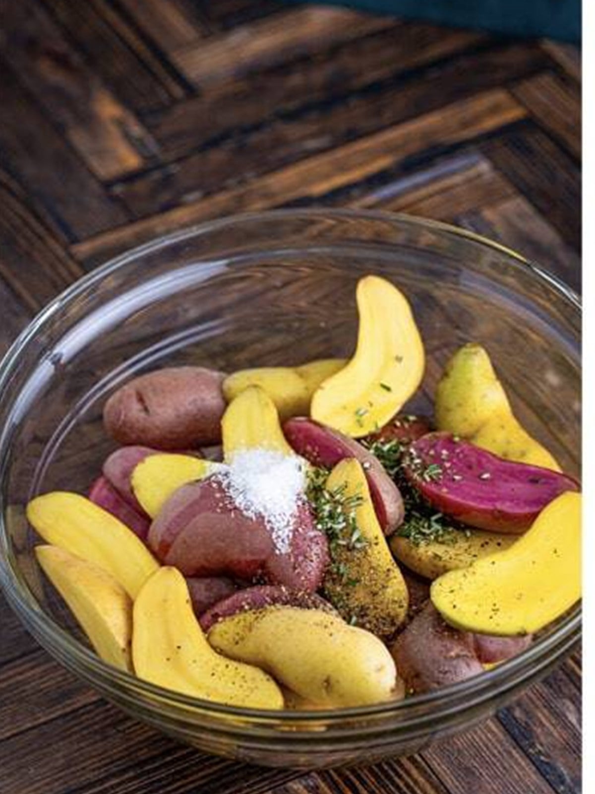 Halved fingerling potatoes in a bowl with olive oil, salt, pepper, and rosemary.