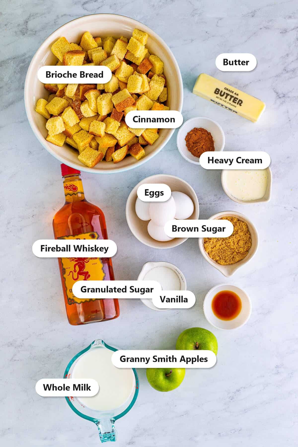 Labeled ingredients for Fireball apple bread pudding including brioche bread, whole milk, Fireball whiskey, apples, eggs, and sugars.
