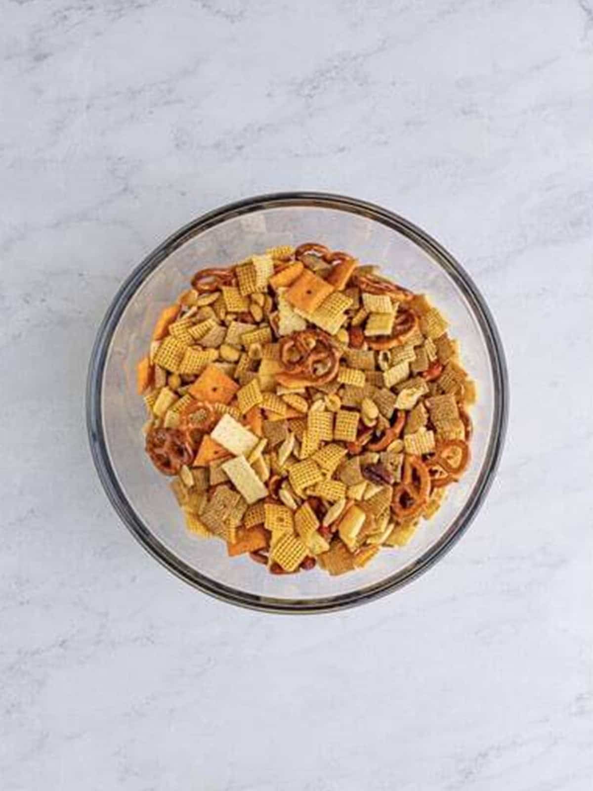 Chex, cheez-its, pretzels, club crackers, and nuts tossed together in a large bowl.