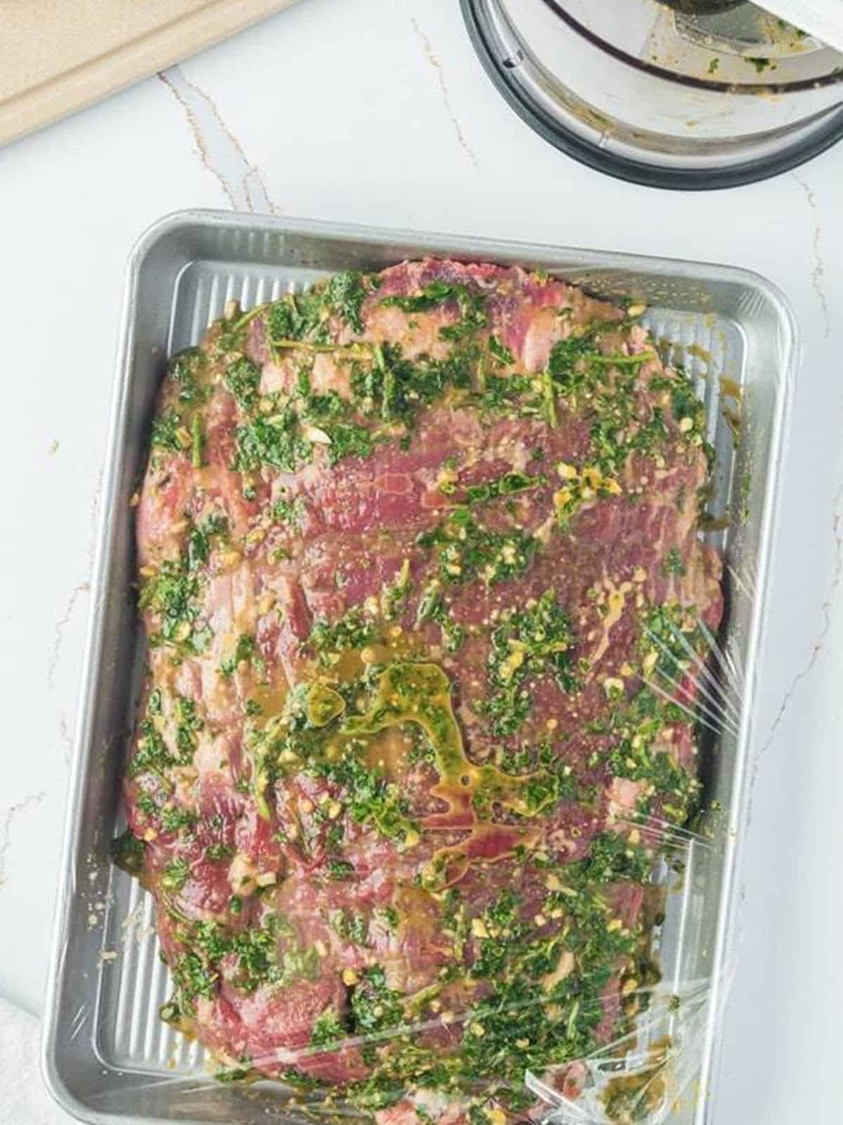 Flank steak coated in the cilantro lime chimichurri marinade on a sheet tray.