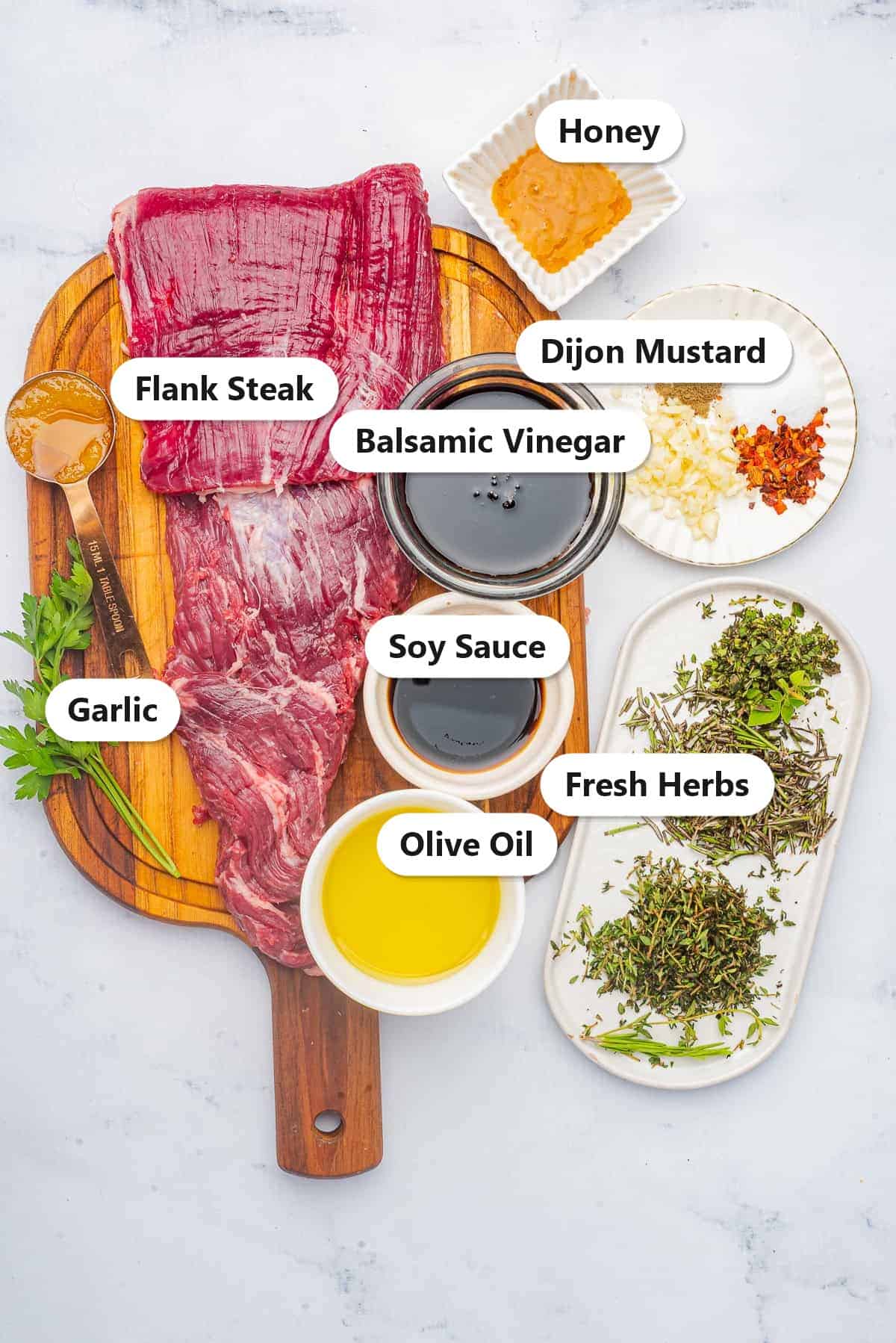 Labeled flank steak marinade ingredients including flank steak, balsamic vinegar, soy sauce, olive oil, honey, and fresh herbs.