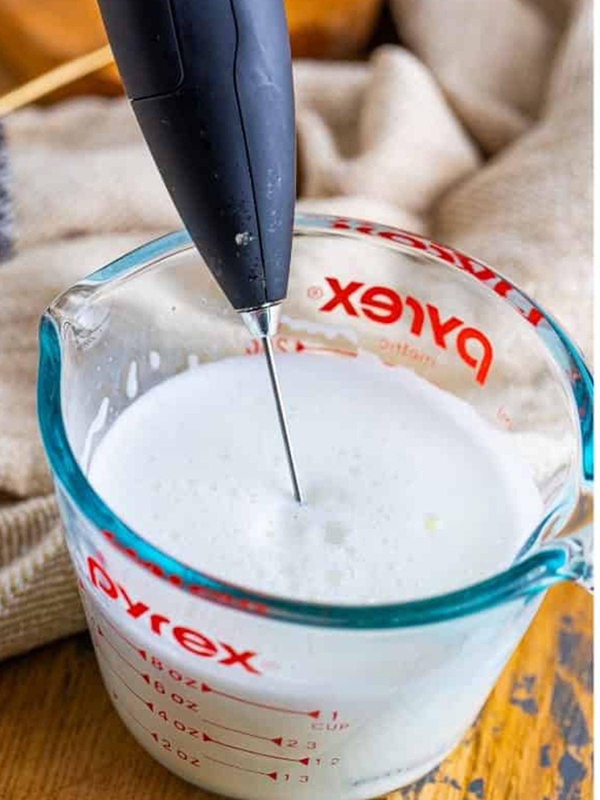 Frothing warm milk with a handheld frother in a measuring cup