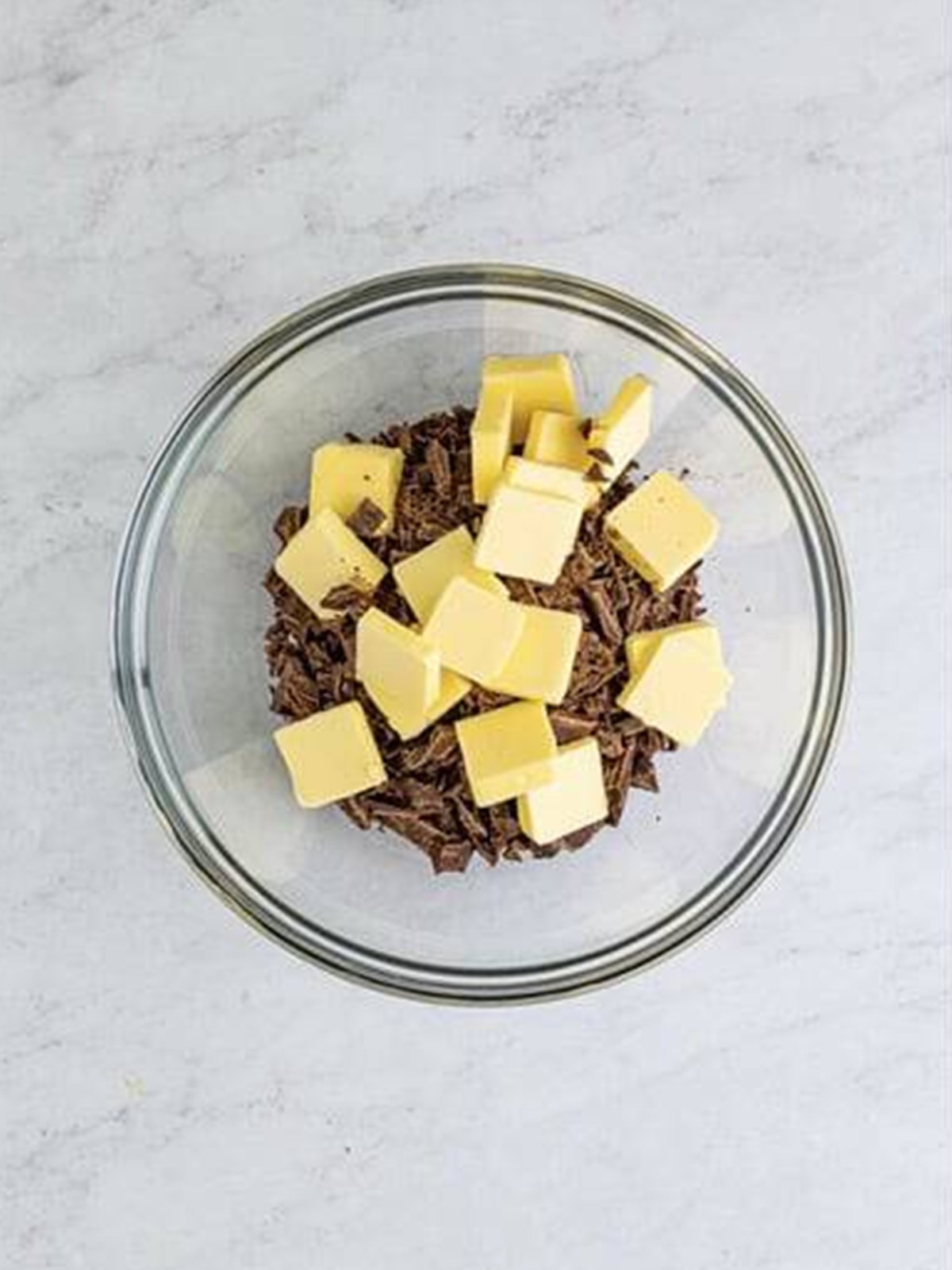 Chopped semi-sweet chocolate and butter in a glass bowl ready to melt for flourless chocolate cake.