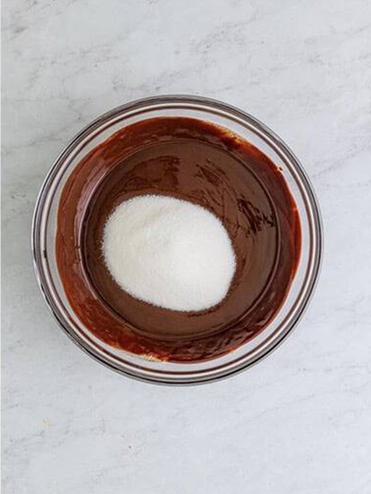 Granulated sugar being whisked into smooth melted chocolate.