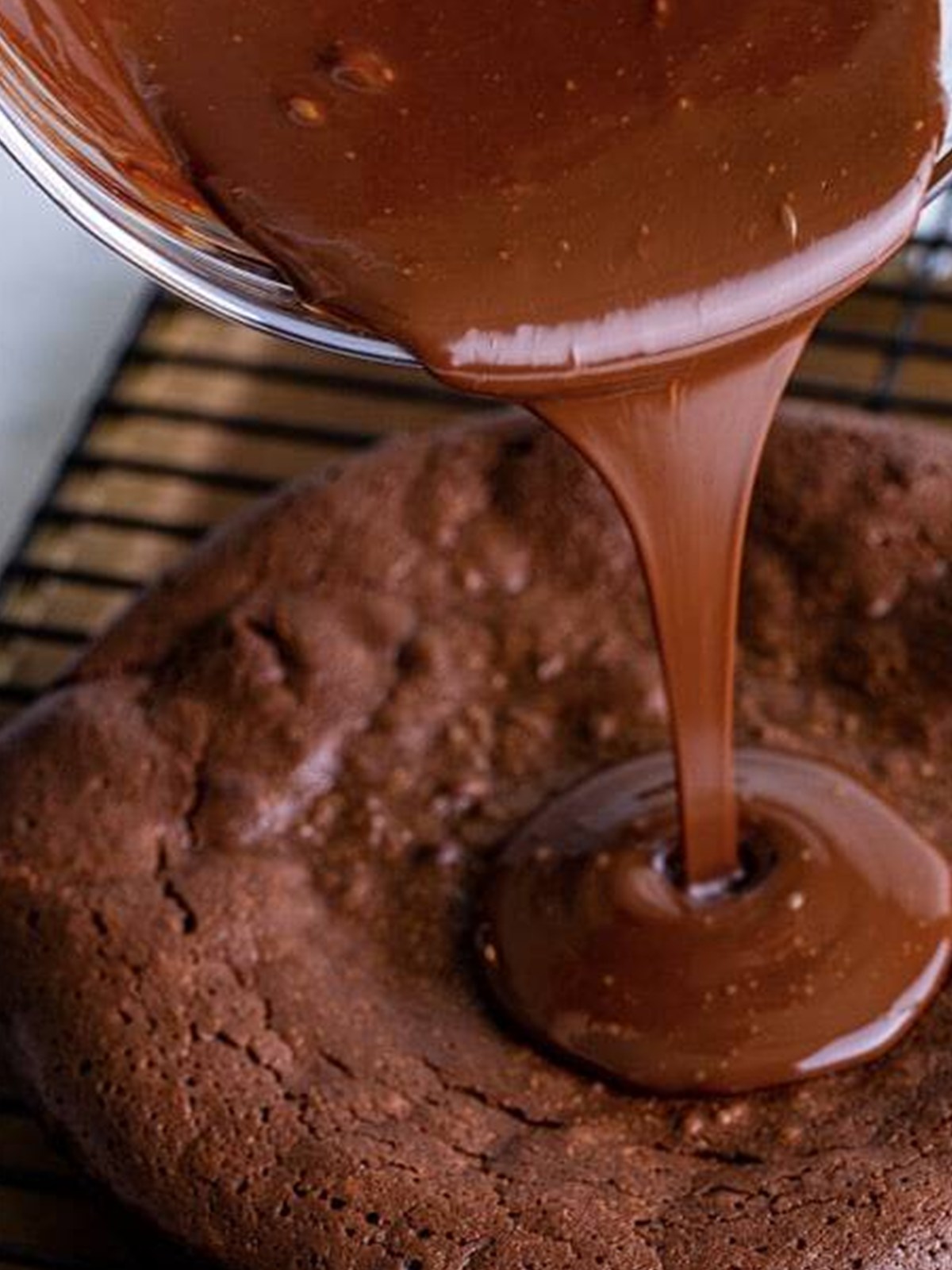 Glossy chocolate ganache being poured over the top of a cooled flourless chocolate cake.