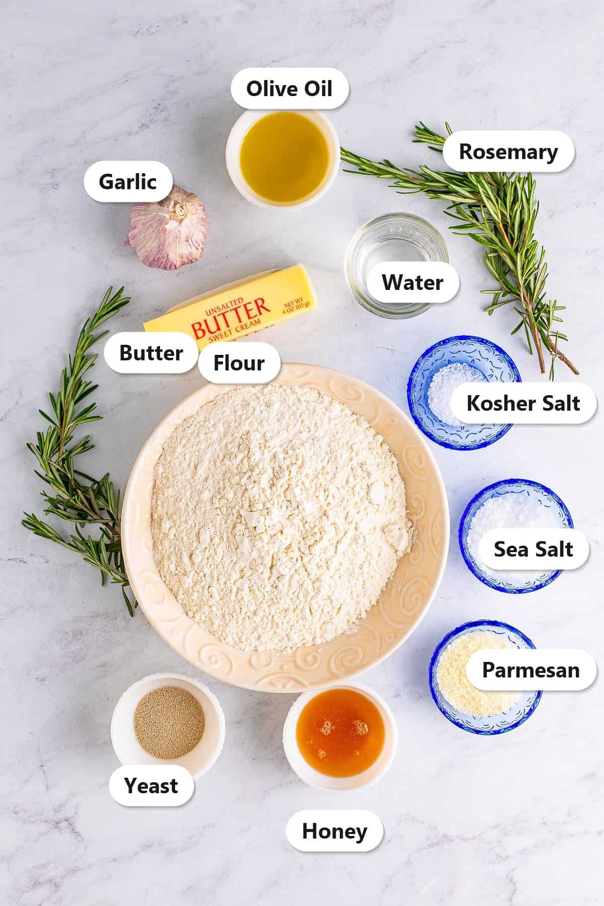 Labeled ingredients for garlic rosemary focaccia bread including flour, yeast, honey, olive oil, water, butter, Parmesan, salt, rosemary, and garlic.