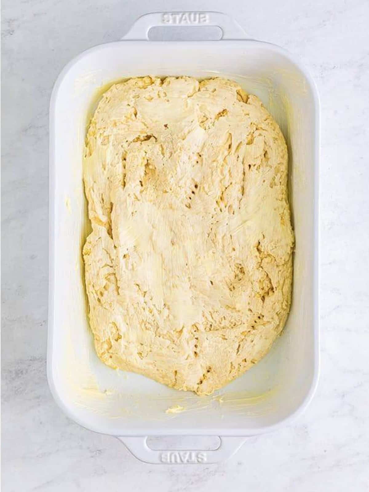 Focaccia dough pressed and spread to fill the buttered baking dish.