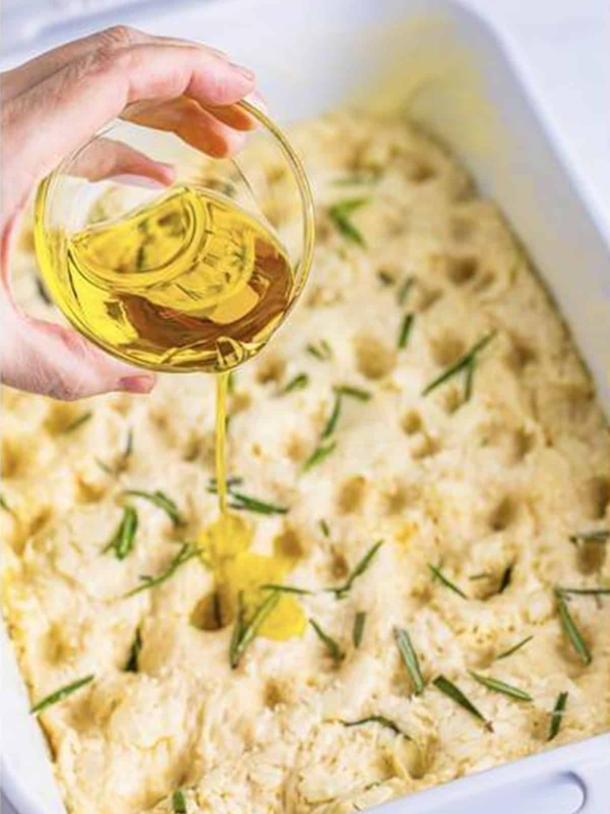 Drizzling olive oil over the dimpled focaccia bread before baking.