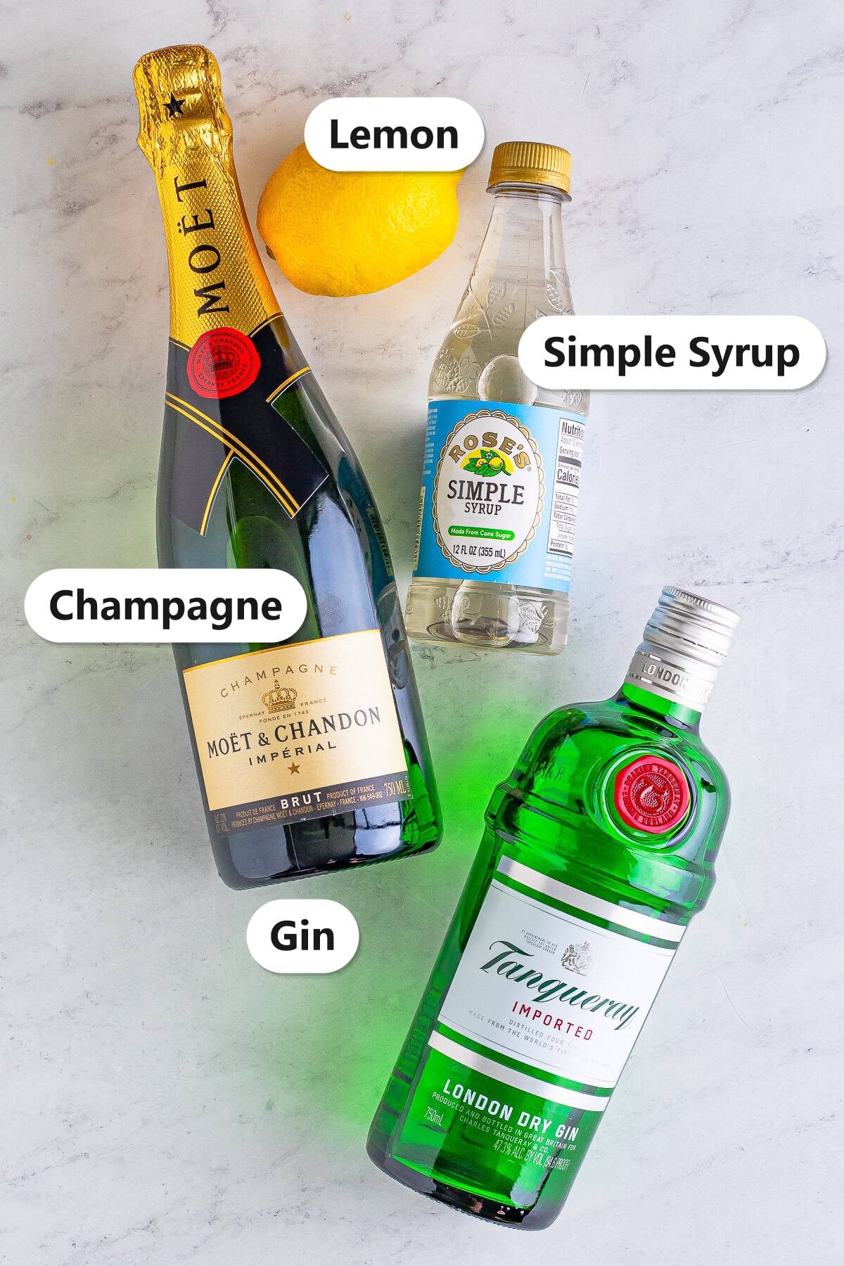 French 75 ingredients labeled on a marble counter: Champagne, Lemon, Simple Syrup, and Gin.