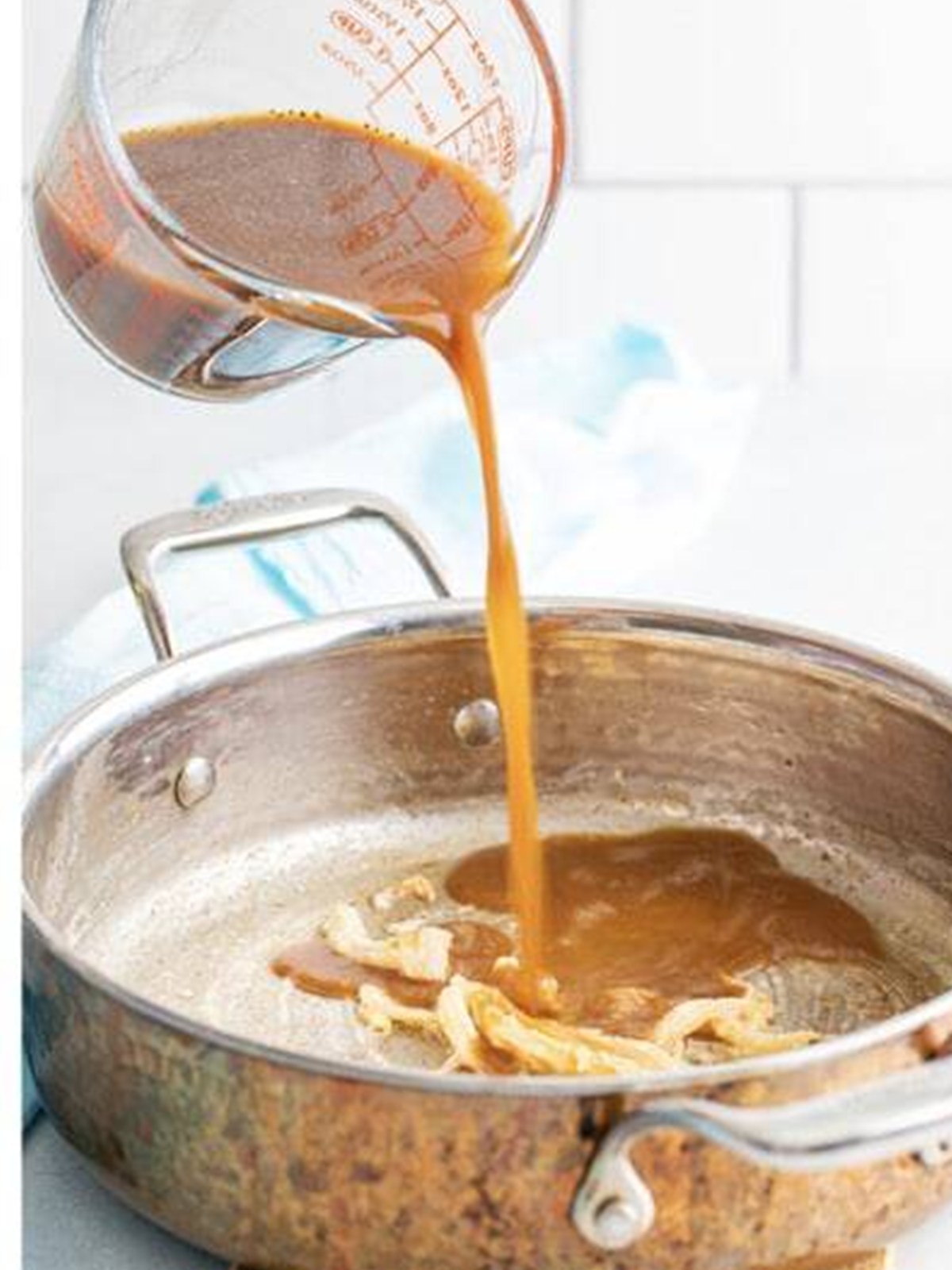 The au jus broth mixture being poured into the skillet with onions and flour.