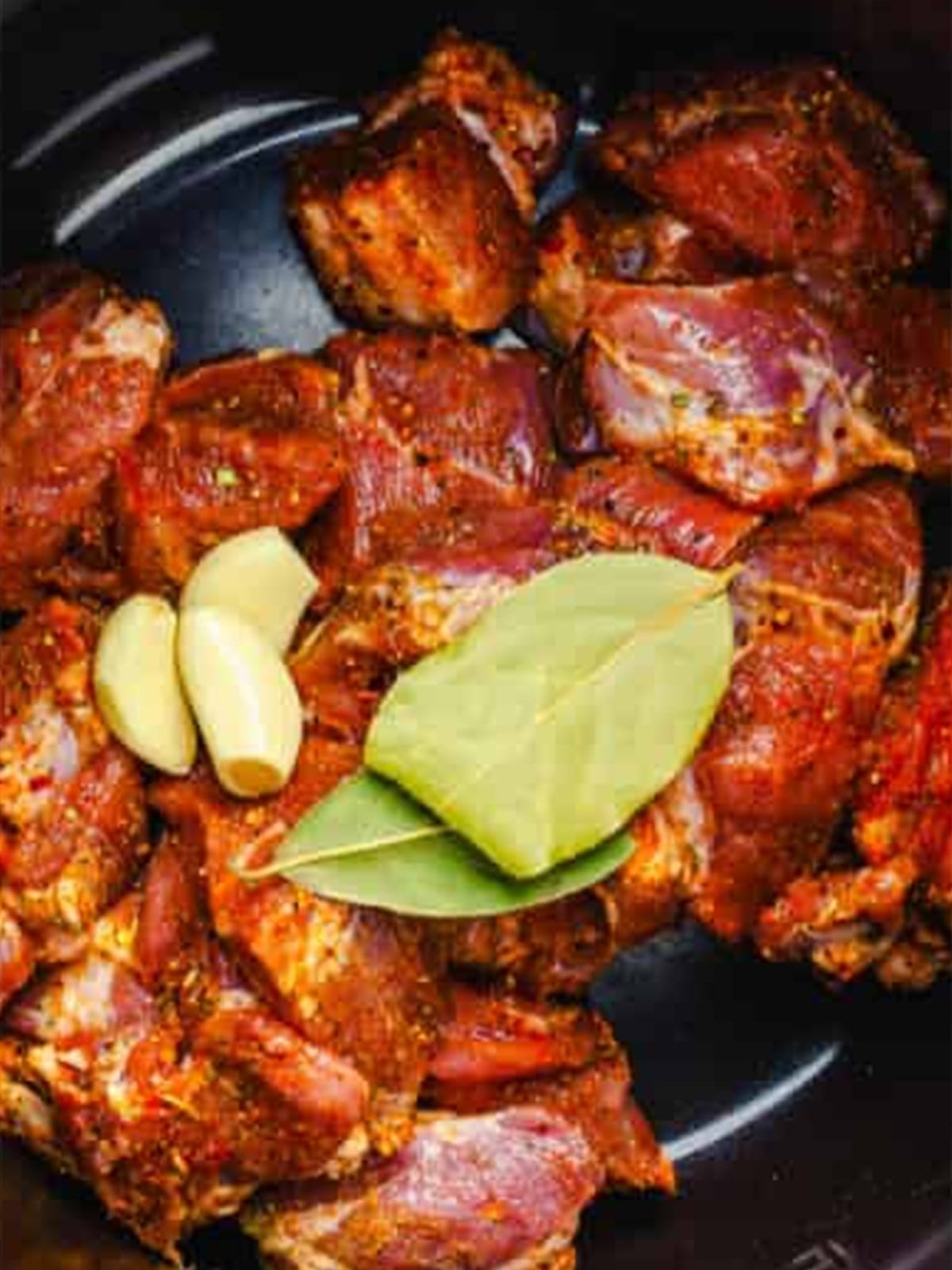 Seasoned beef in a crockpot with bay leaves and garlic