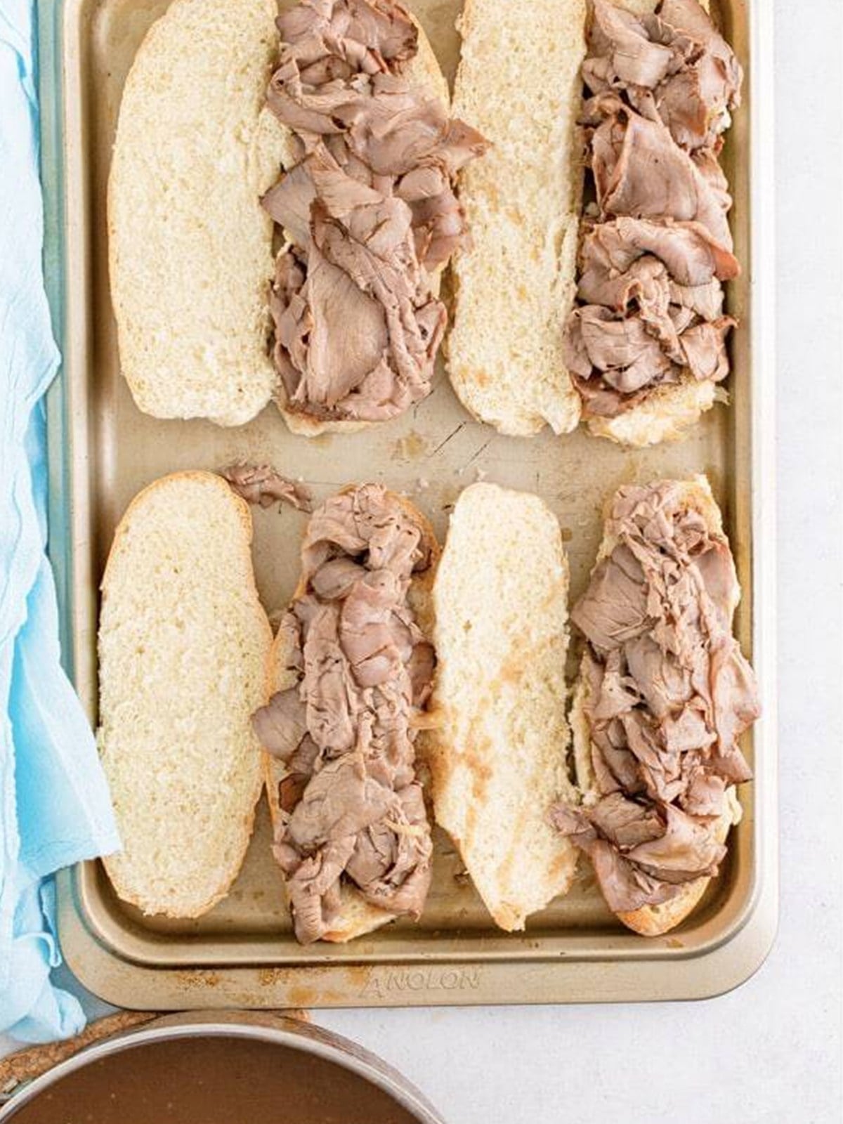 Warm roast beef piled onto split hoagie rolls on a baking tray.