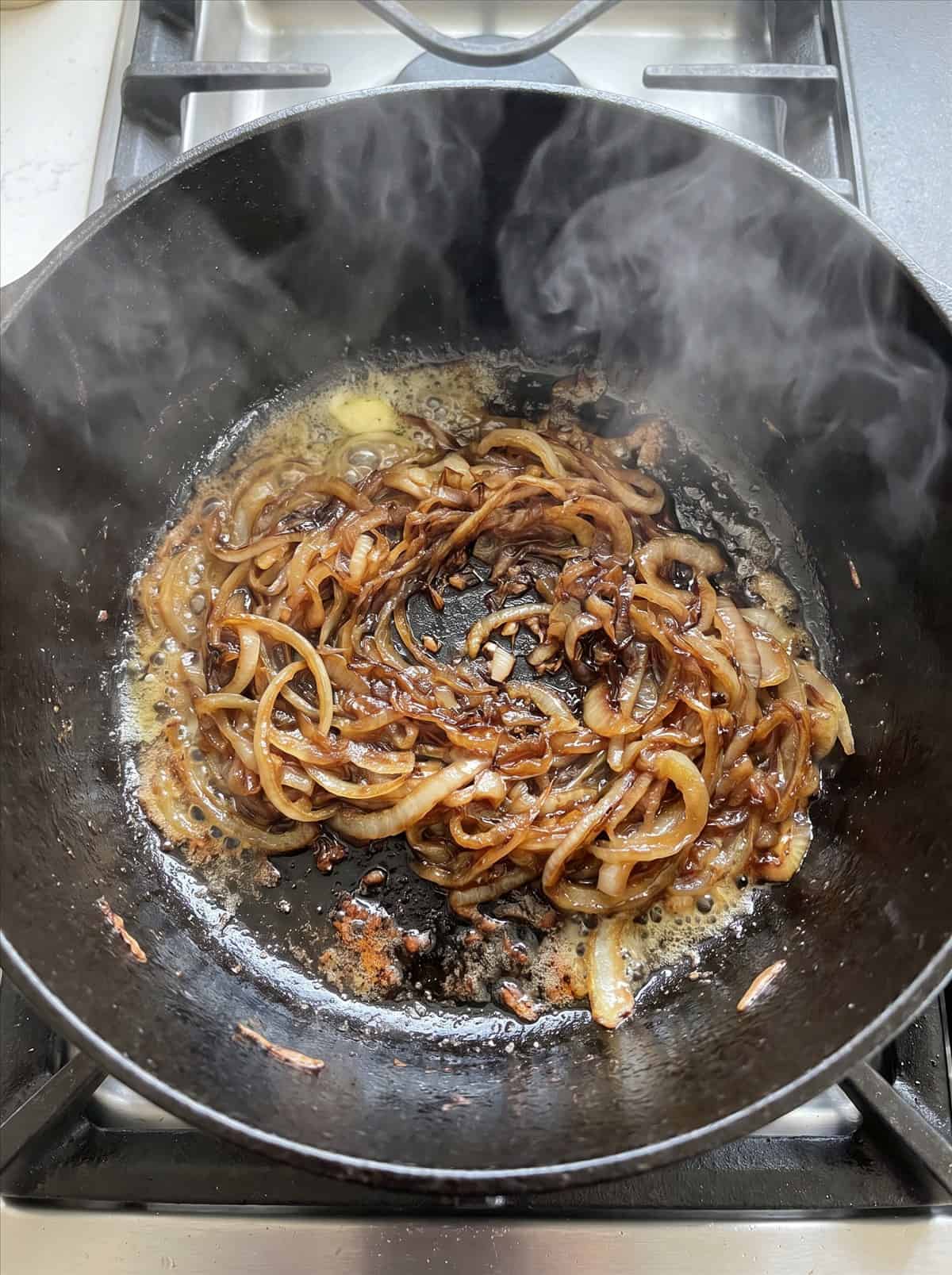 Deeply caramelized golden brown onions cooking in butter in a black Dutch oven.