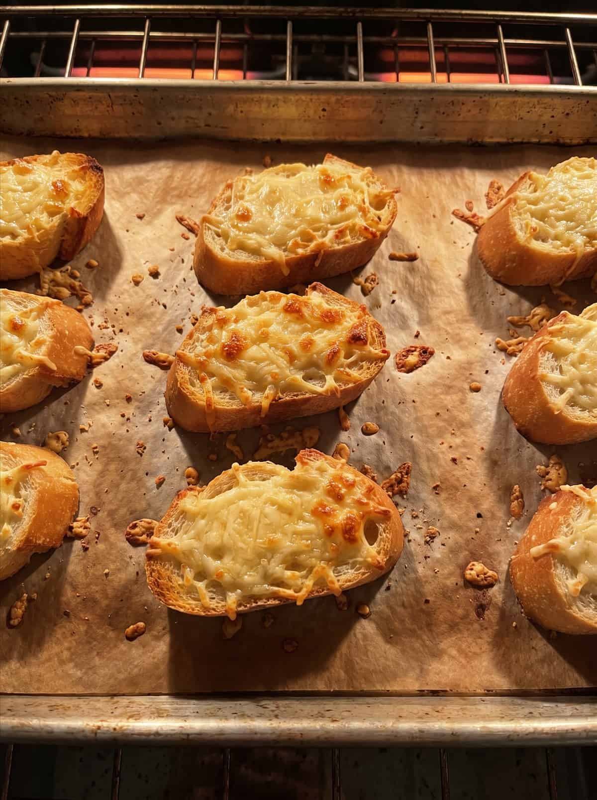 Baguette slices topped with melted bubbly gruyere cheese on a baking sheet.