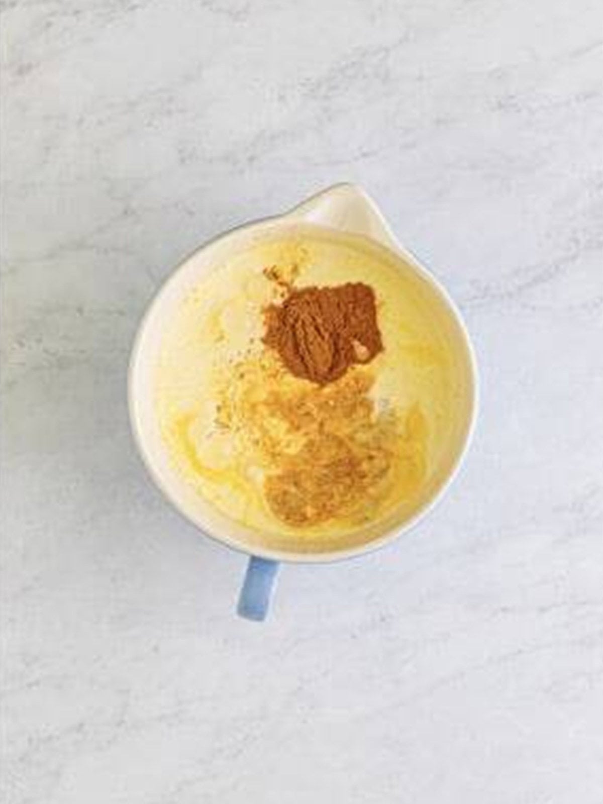 Eggs, milk, cream, sugar, and cinnamon whisked into a custard in a measuring cup.