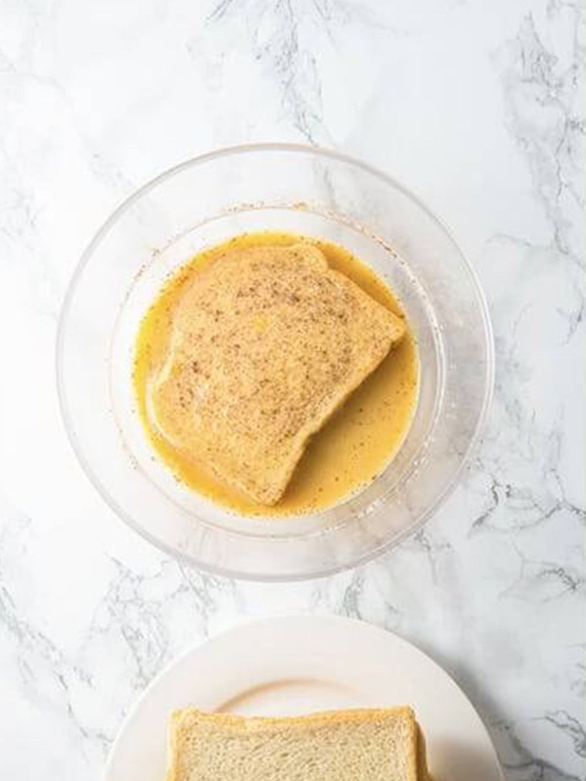 A slice of bread being dipped into the egg and milk custard for French toast.