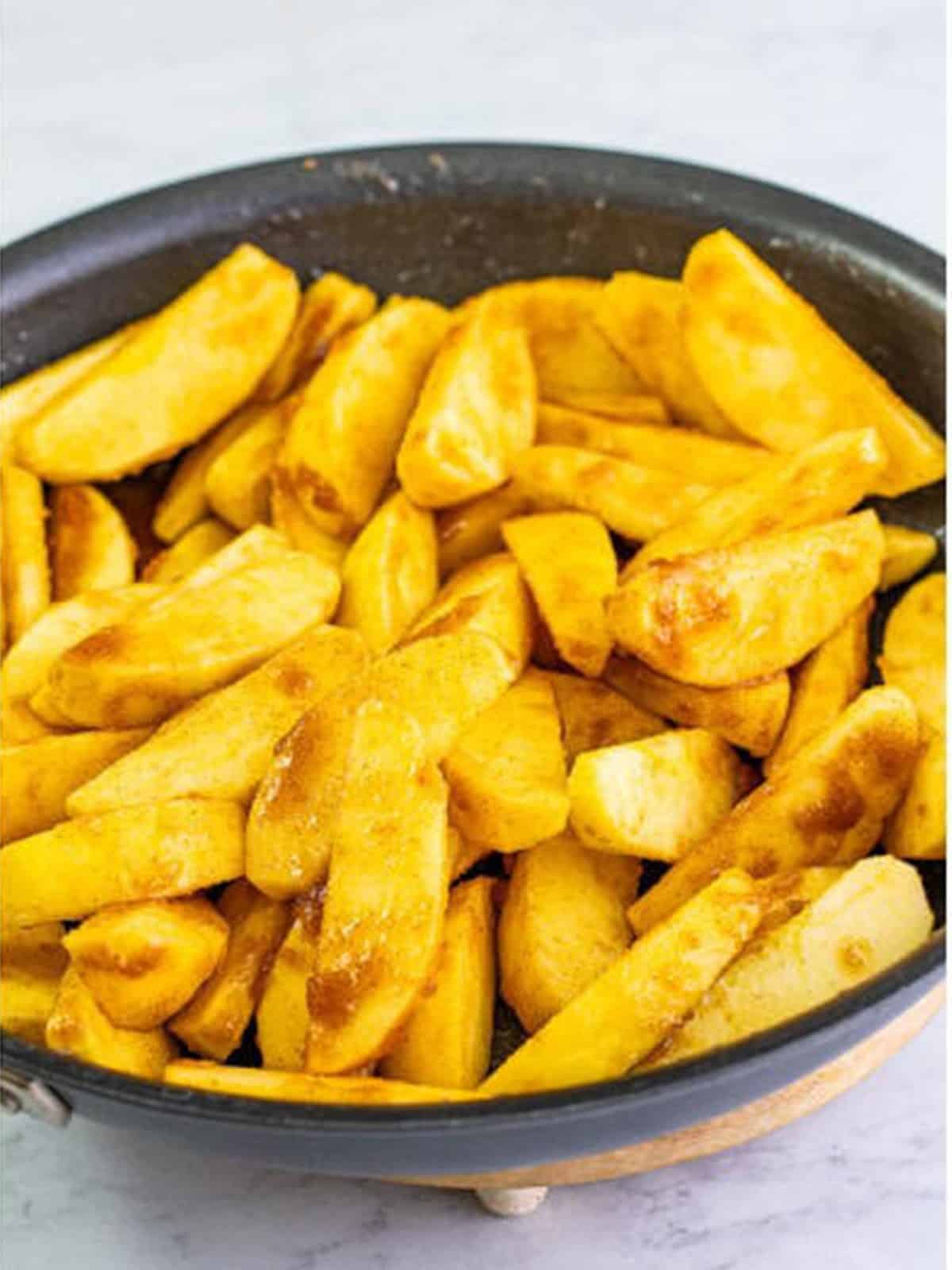 Apple slices coated in the cinnamon sugar mixture and simmering in the skillet.
