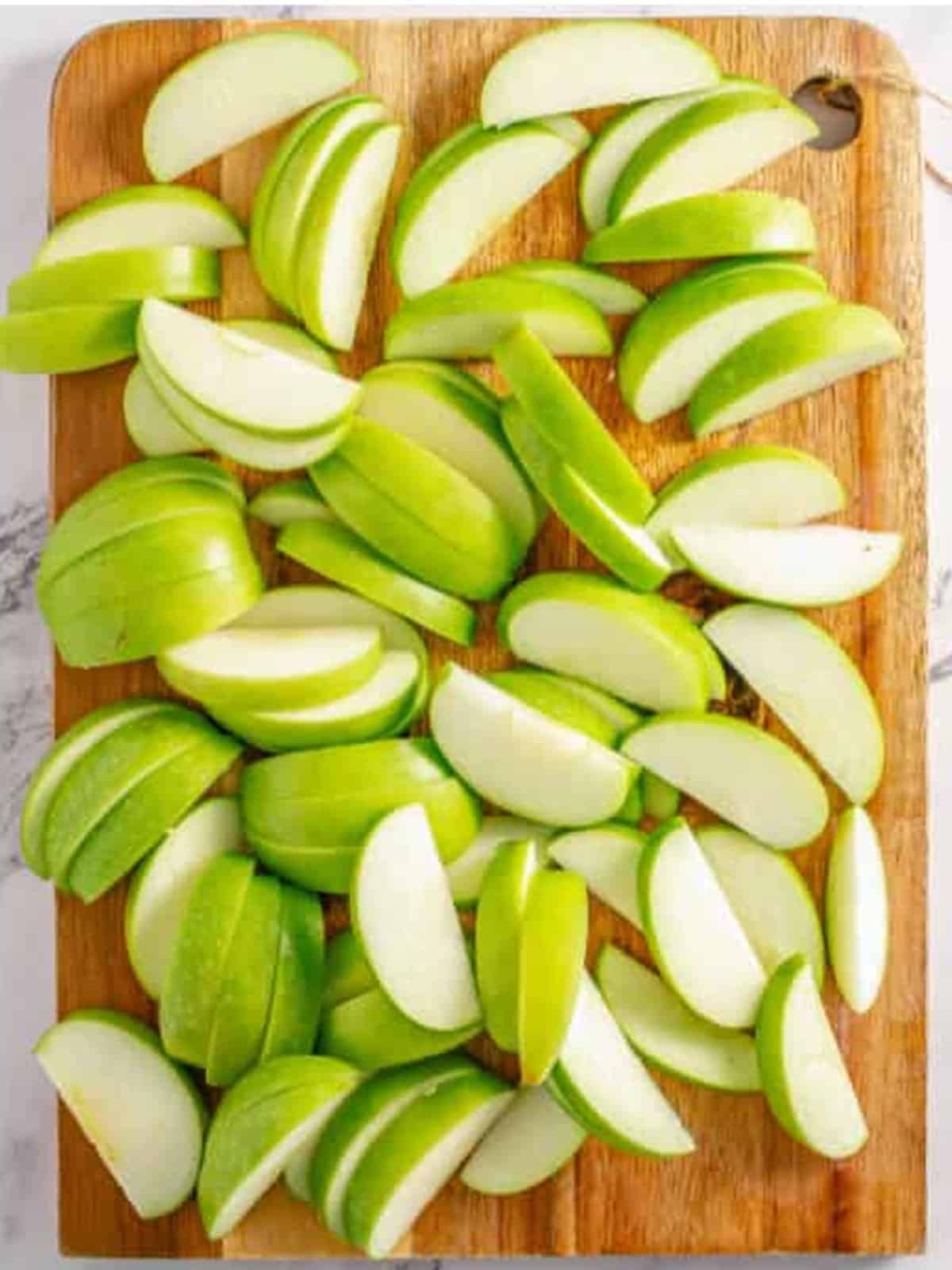 Sliced granny smith apples on a wooden cutting board for fried apples.