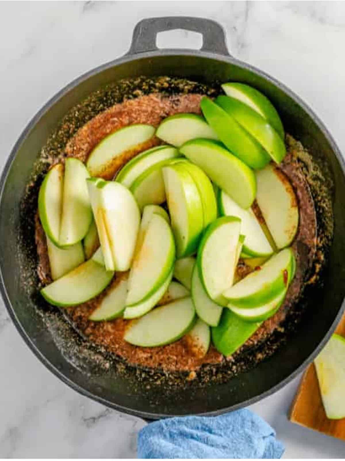 Adding sliced apples to the cinnamon butter mixture in a skillet.