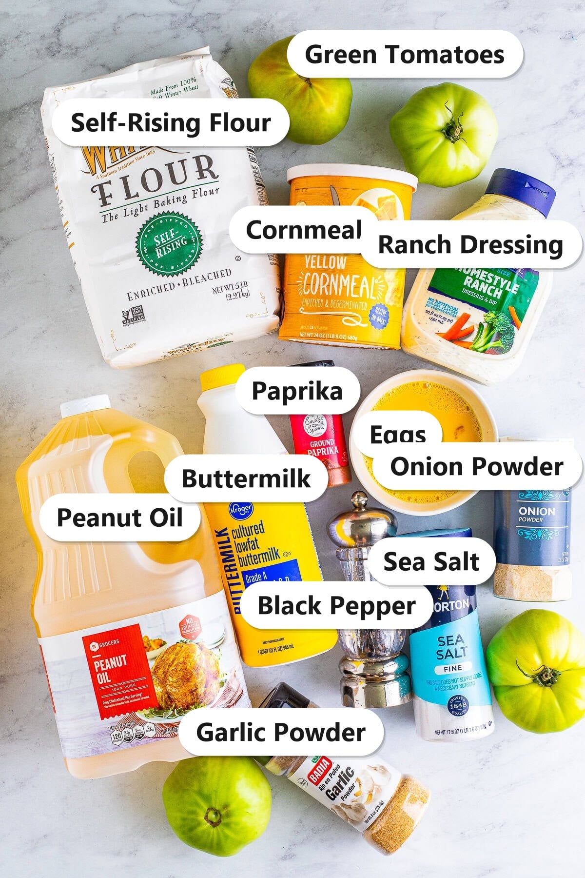 Ingredients needed to make fried green tomatoes labeled on a marble counter.