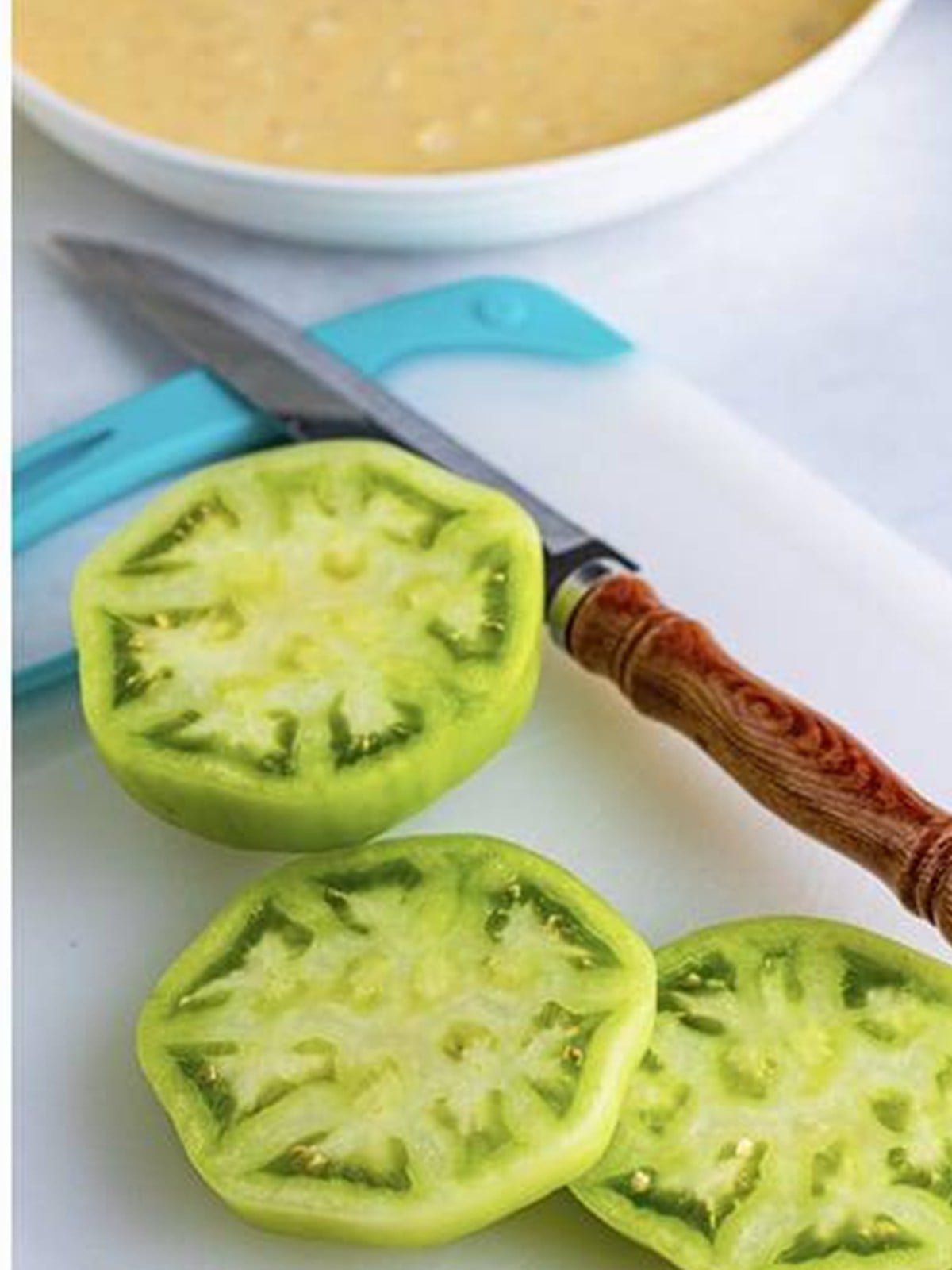 Green tomatoes sliced into thick rounds next to a knife.