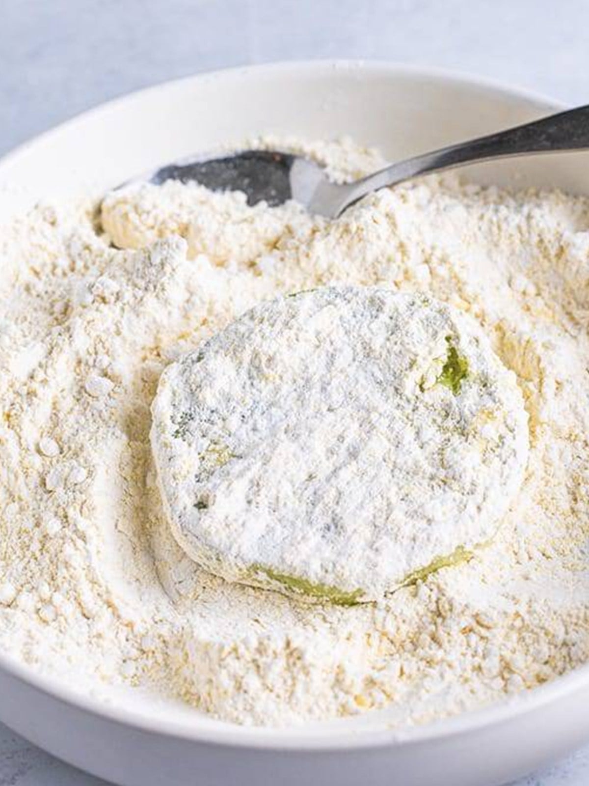 A battered green tomato slice being coated in the flour and cornmeal mixture.