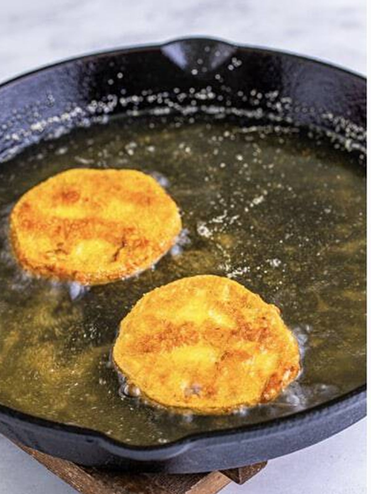 Green tomato slices frying in hot oil in a cast iron skillet.