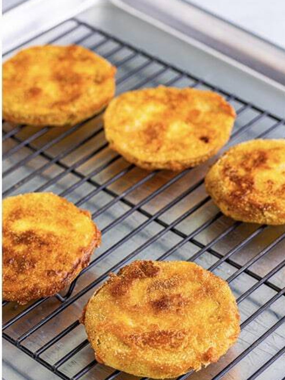 Golden brown fried green tomatoes draining on a wire rack.