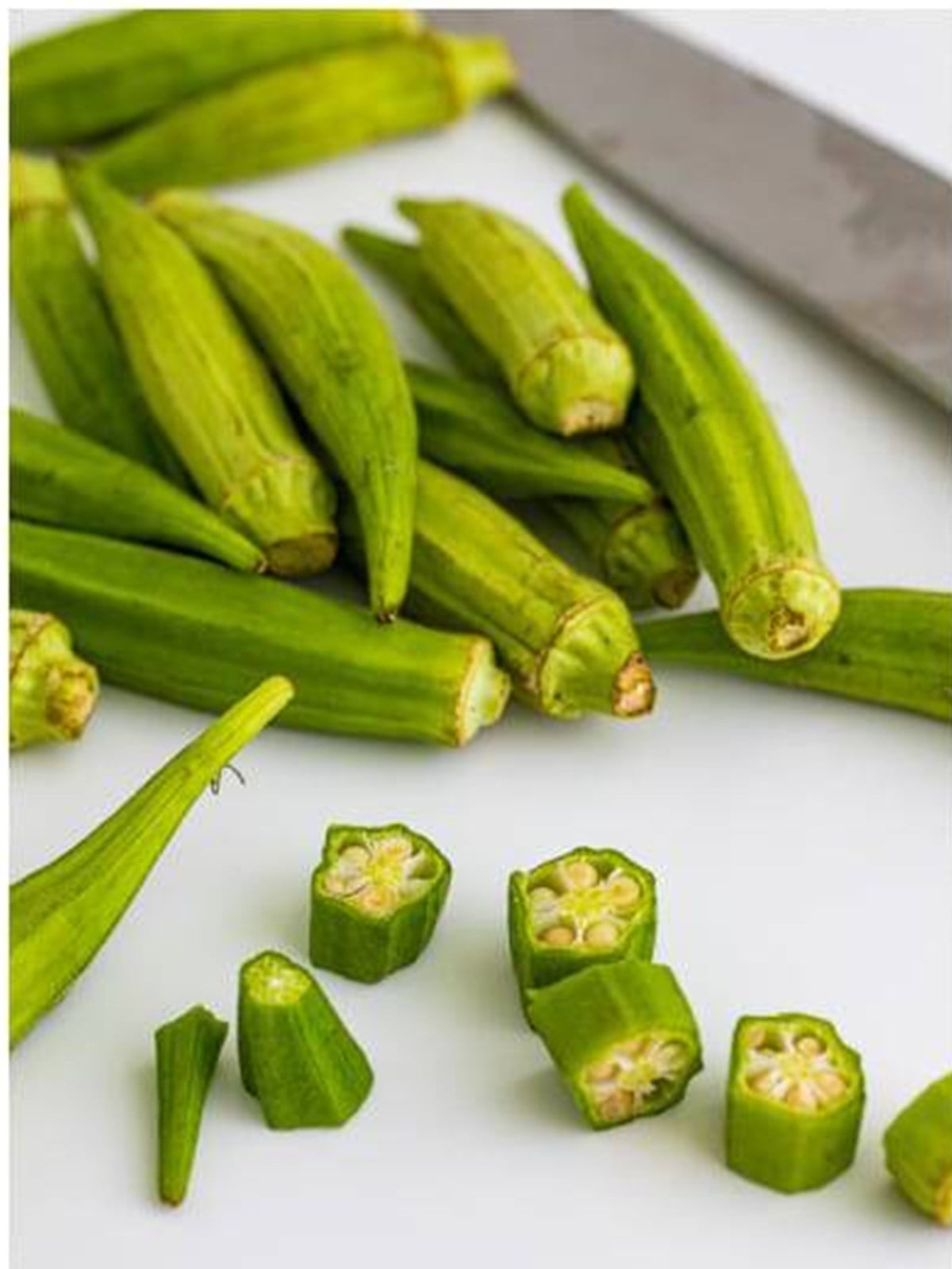 Fresh okra pods being sliced into rounds on a cutting board for fried okra.
