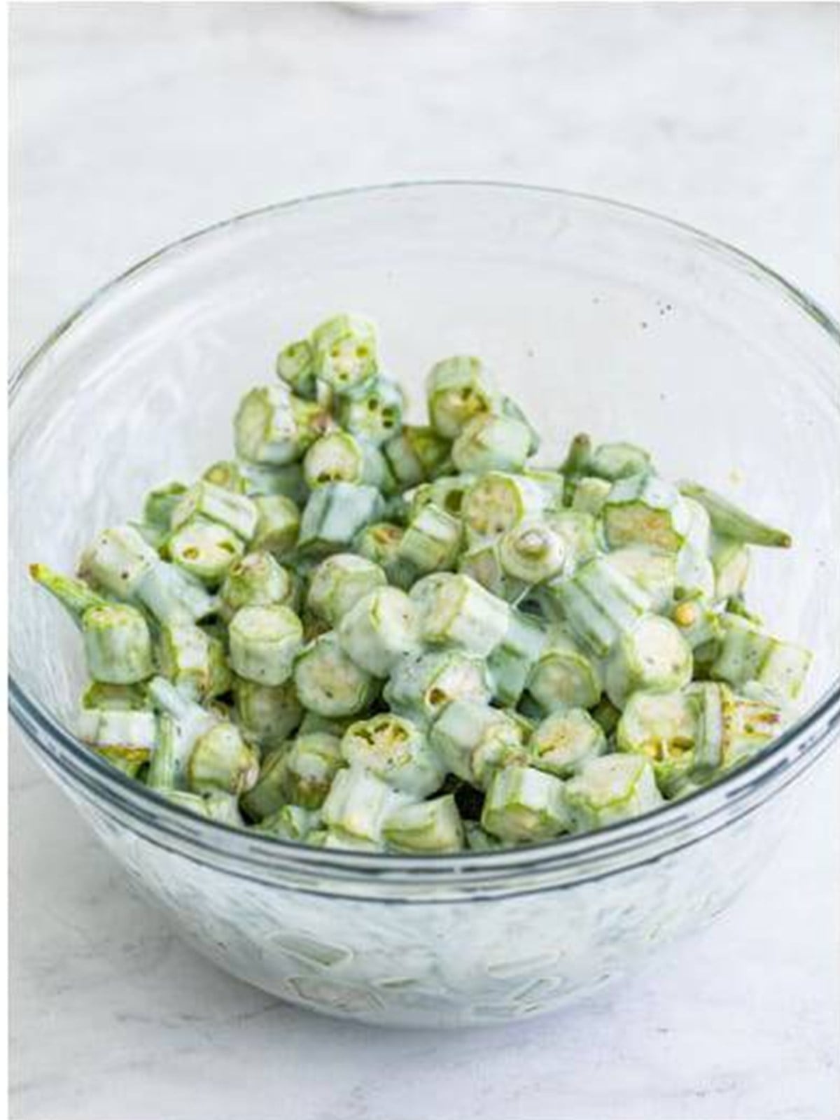 Sliced okra soaking in seasoned buttermilk in a glass bowl for fried okra.