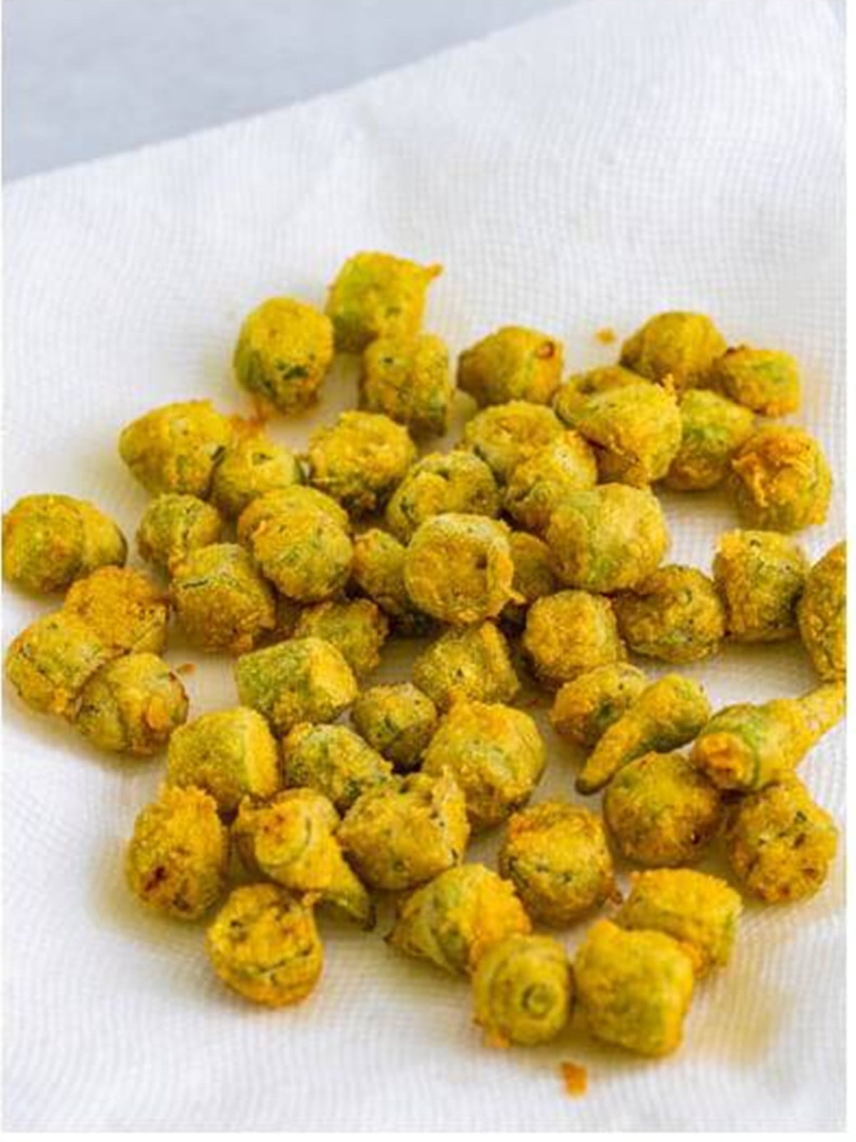 Golden crispy fried okra draining on a paper towel after frying.