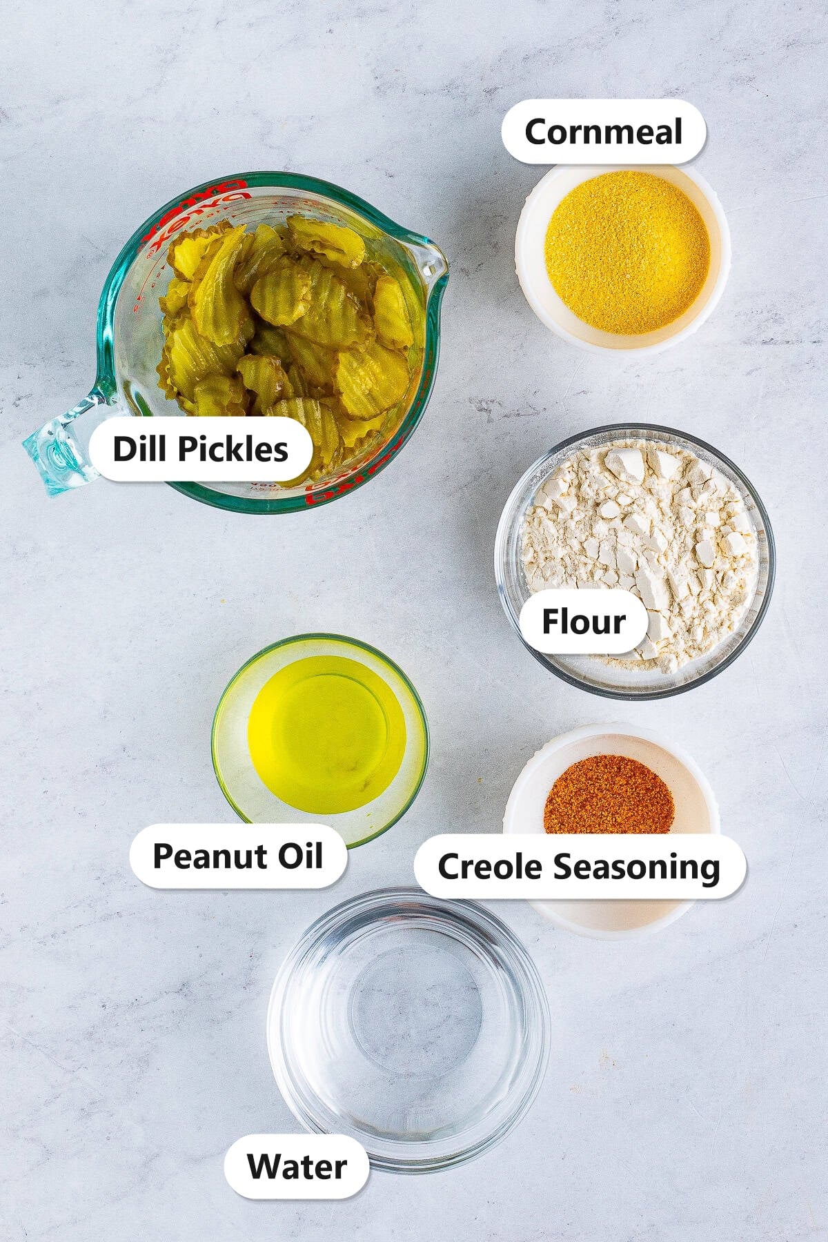 Labeled ingredients to make fried pickles including dill pickle chips, cornmeal, flour, peanut oil, Creole seasoning, and water.