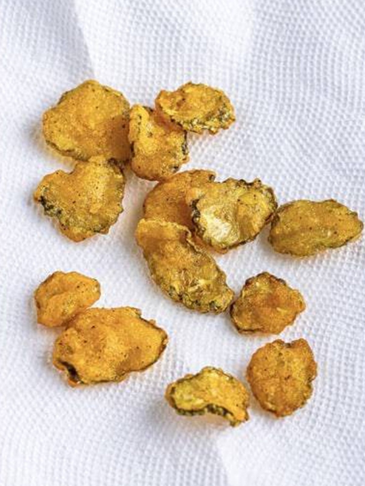 Golden fried pickles draining on a paper towel lined plate.