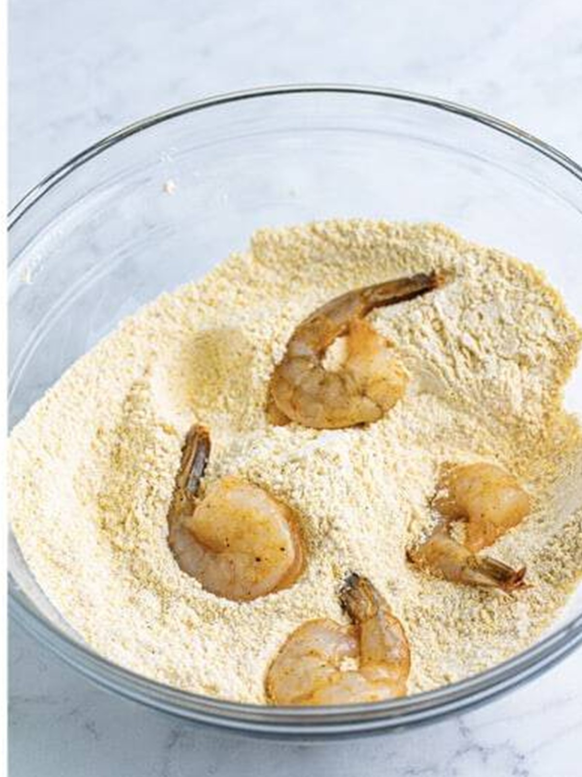 Dredging the shrimp in the cornmeal mixture until well coated for Fried Shrimp.