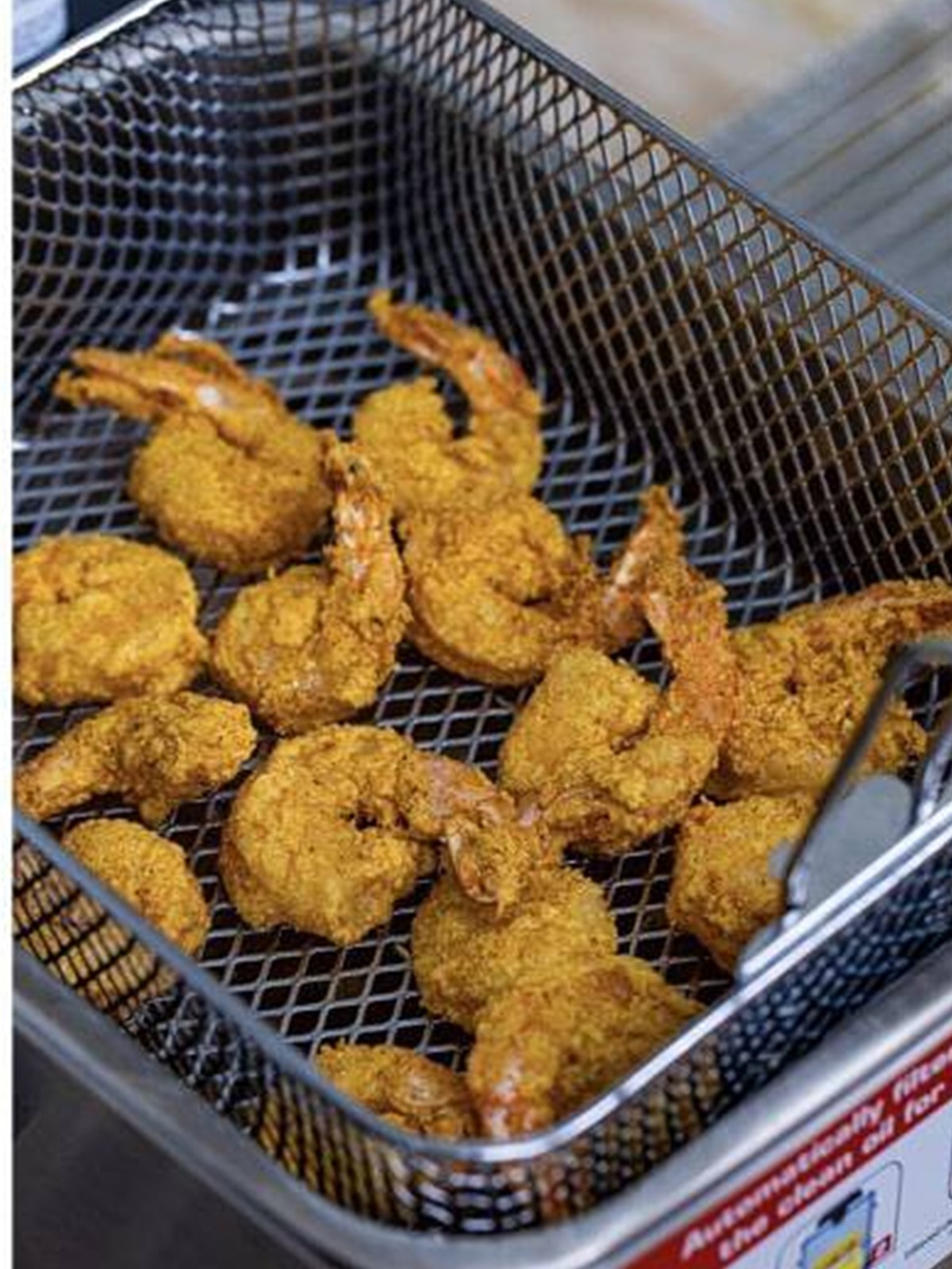Crispy golden Fried Shrimp draining in a fryer basket.