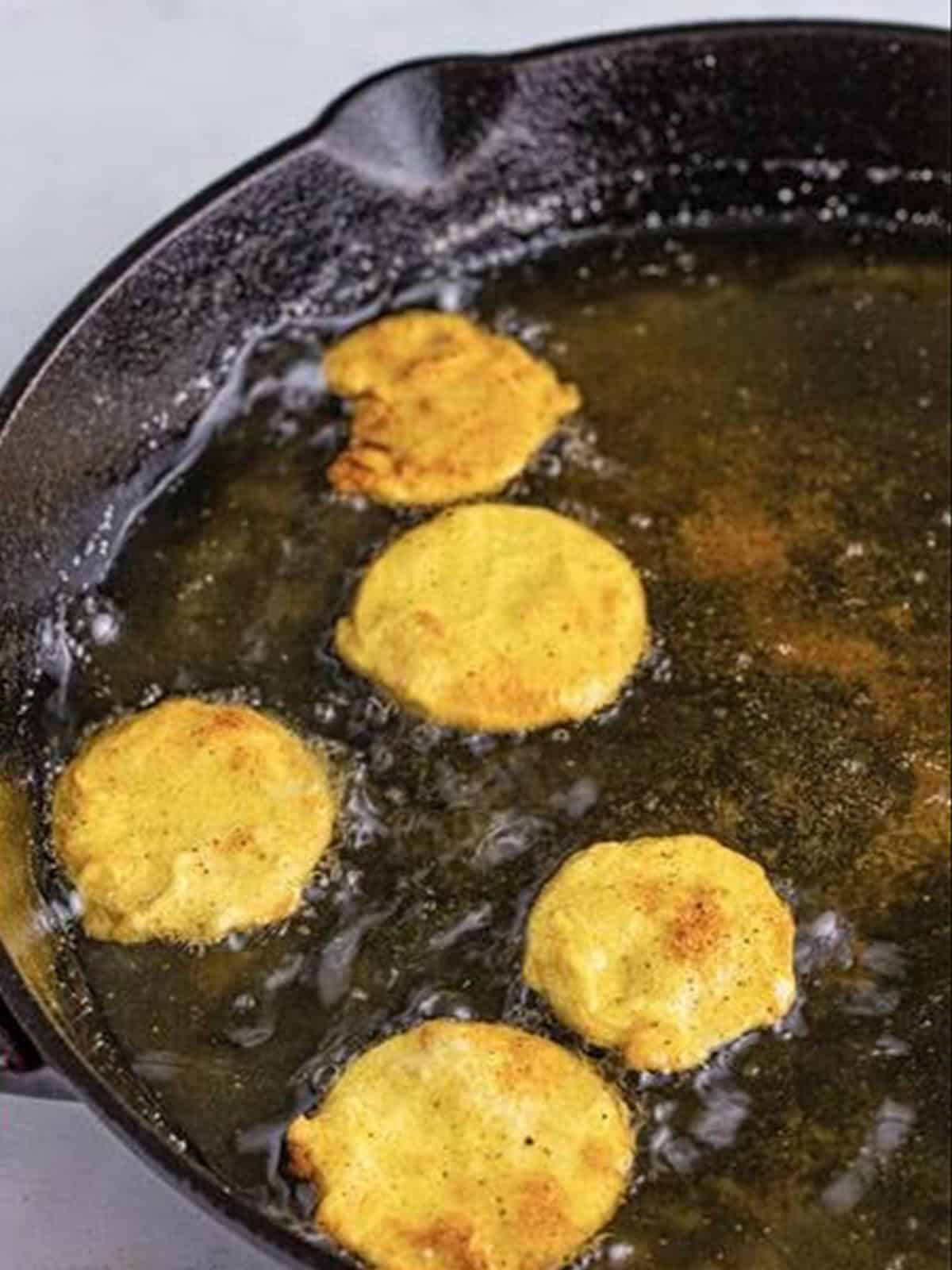 Breaded squash rounds frying to golden brown in a cast iron skillet.