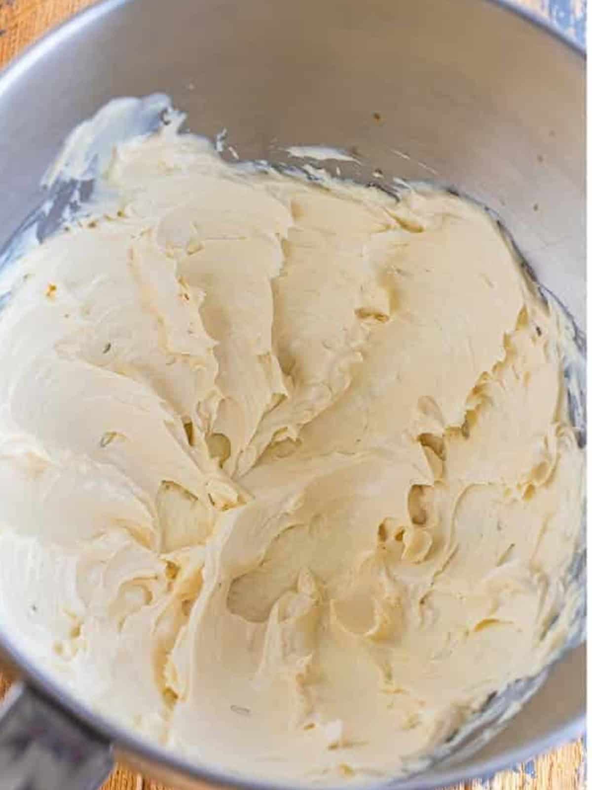 Cream cheese whipped smooth in a stand mixer bowl for whipped cream cheese frosting.