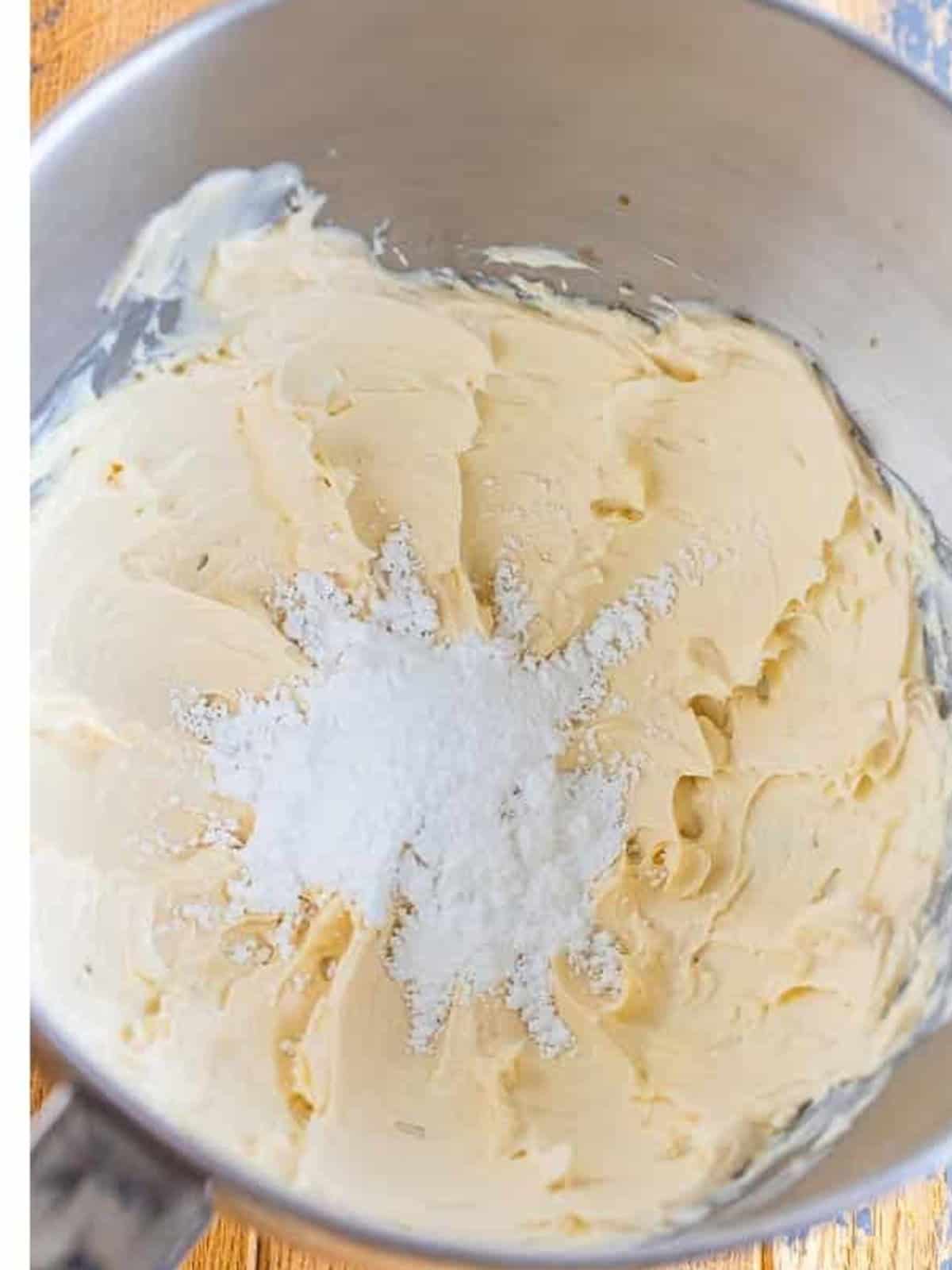 Powdered sugar added to the whipped cream cheese in a mixer bowl.
