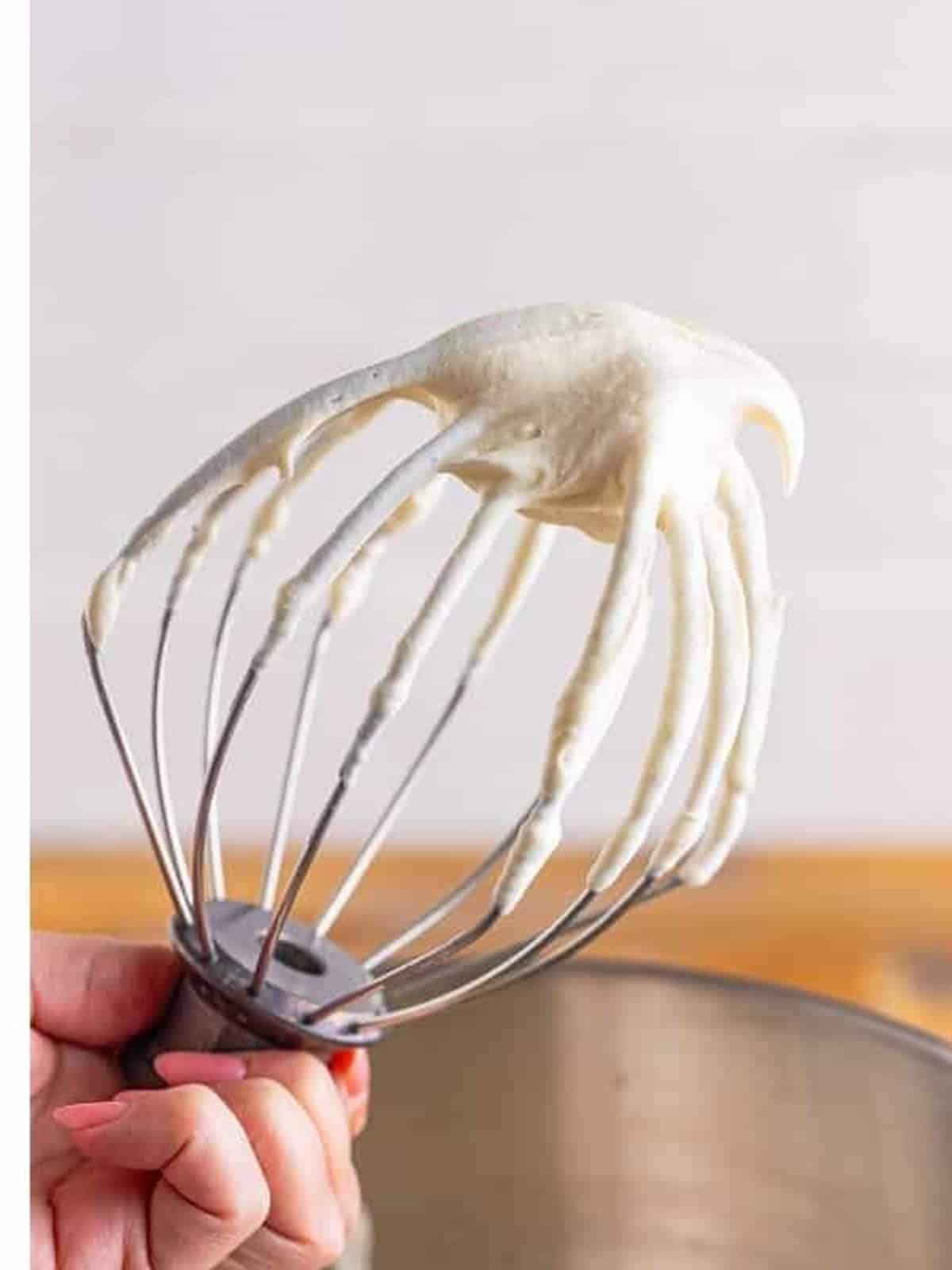 Stiff peaks of whipped cream cheese frosting on a stand mixer whisk.
