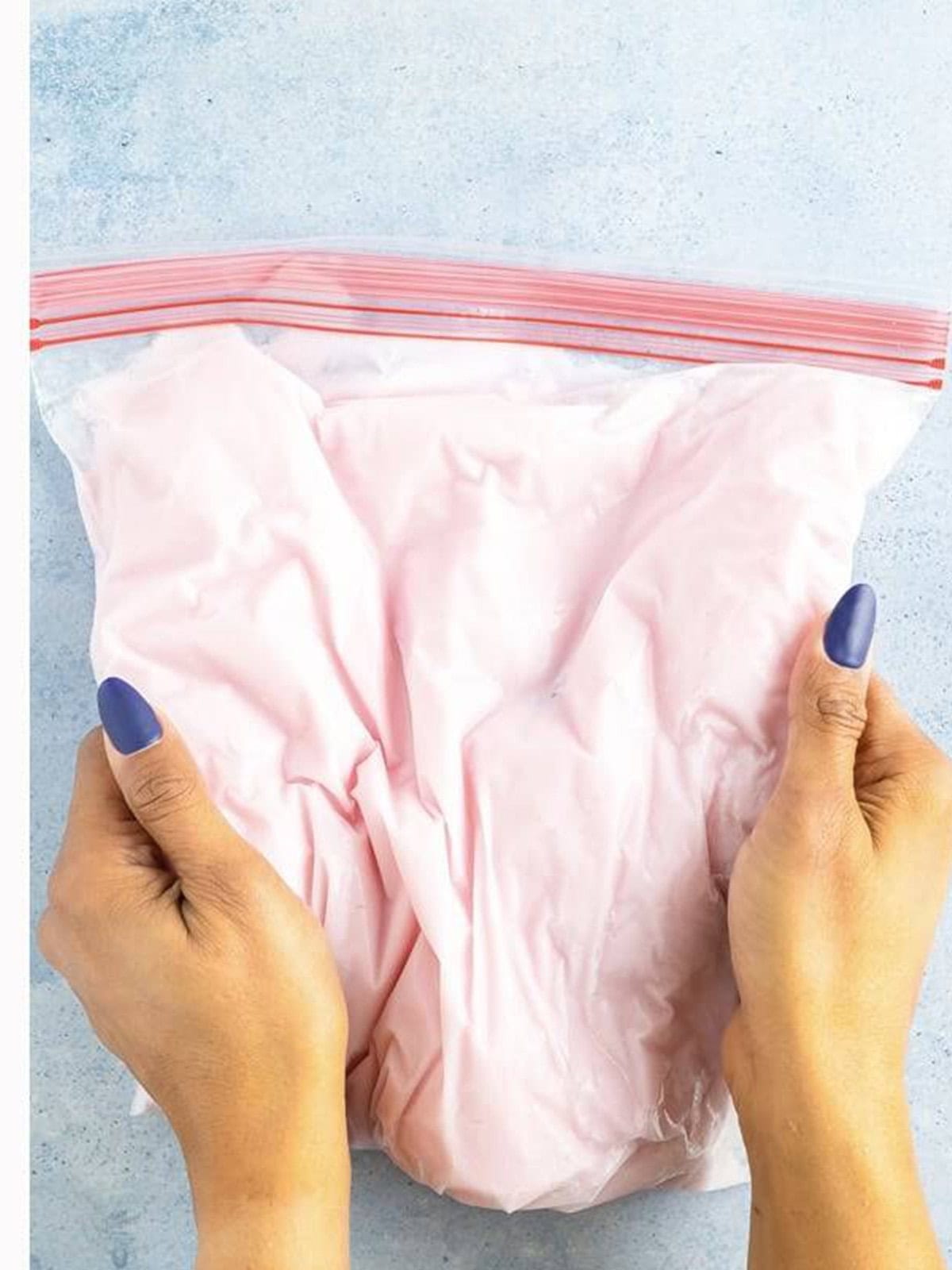 Hands smushing the frozen yogurt in a zip top bag to break up icy bits.