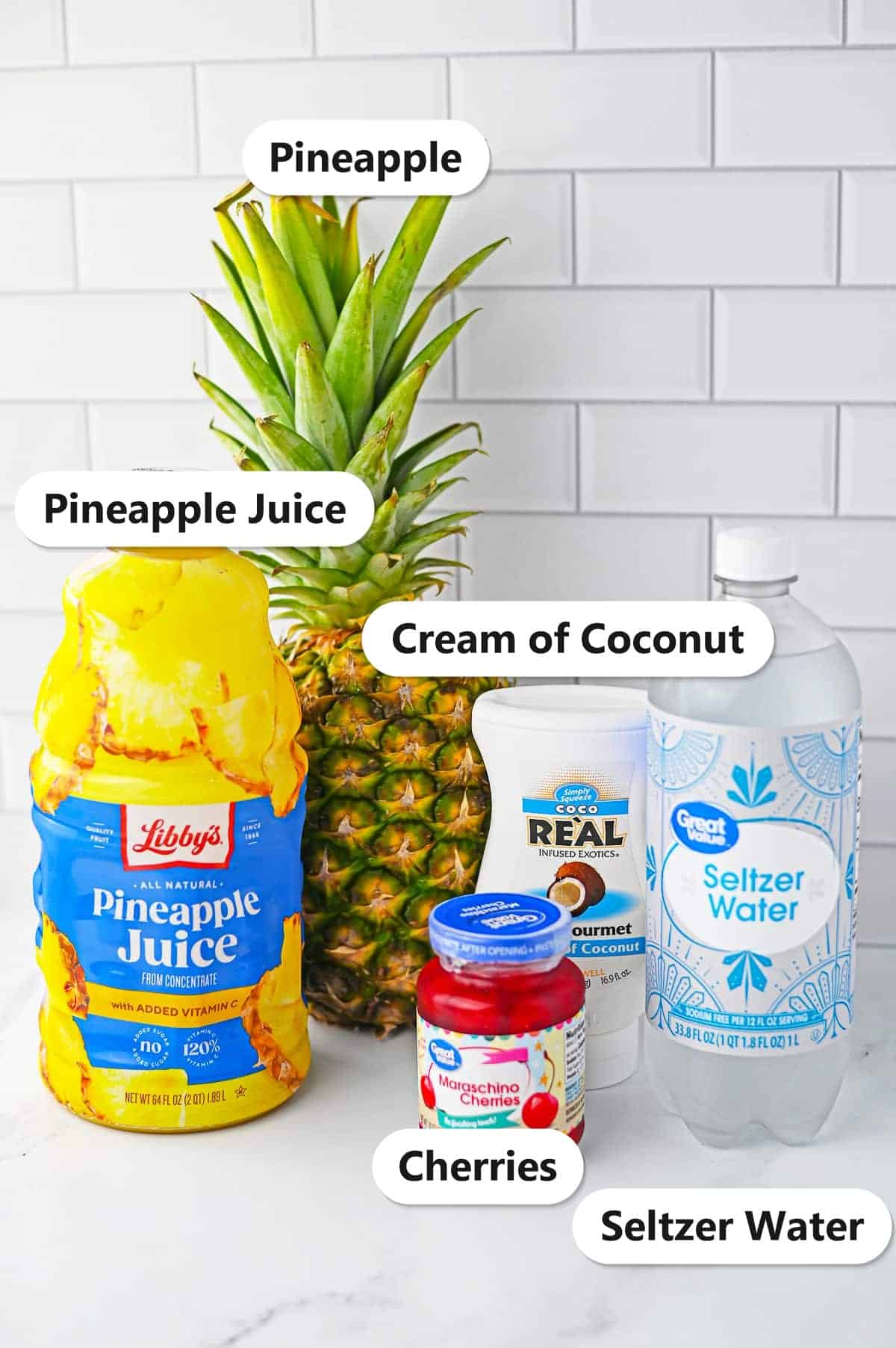 Labeled ingredients for fruit punch recipe including pineapple juice, cream of coconut, seltzer water, fresh pineapple, and maraschino cherries.