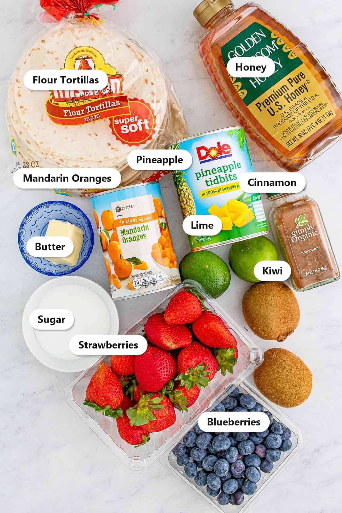 Ingredients to make fruit salsa including strawberries, blueberries, pineapple, mandarin oranges, kiwi, lime, honey, flour tortillas, butter, sugar, and cinnamon.