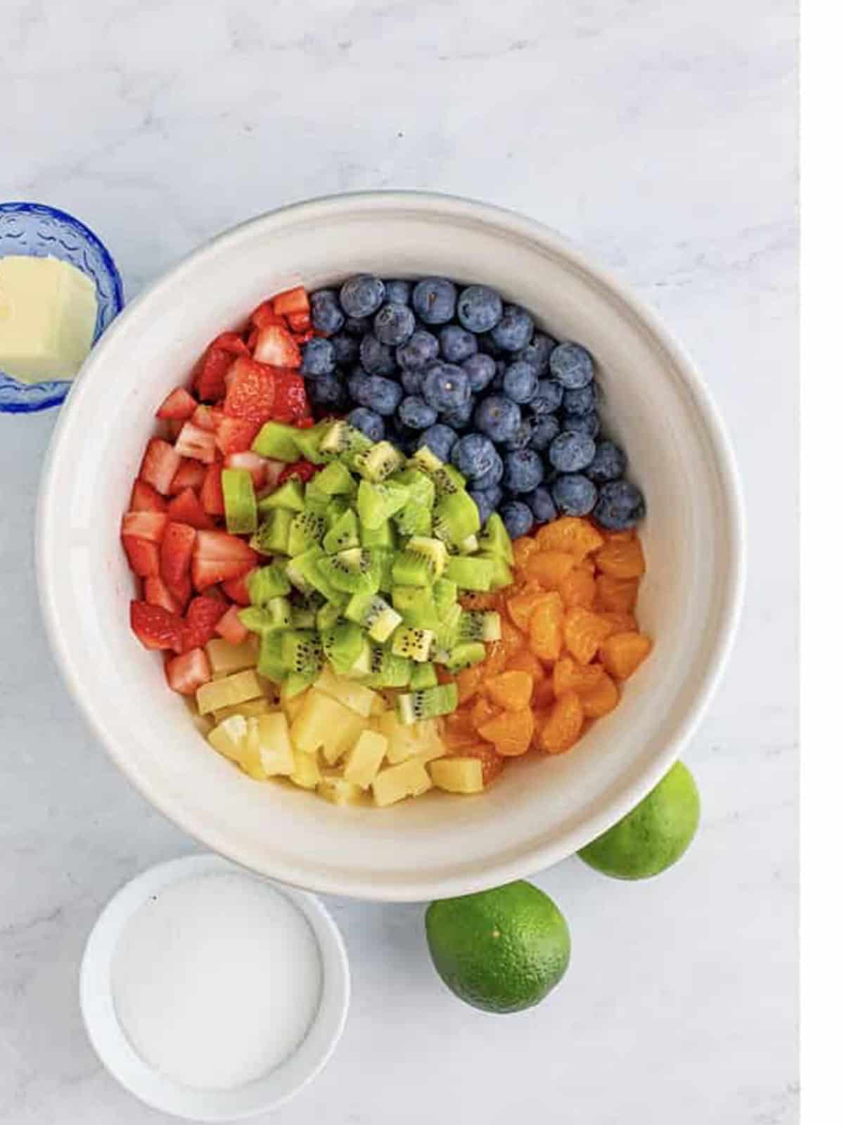 Diced strawberries, blueberries, pineapple, mandarin oranges, and kiwi in a large white bowl for fruit salsa.