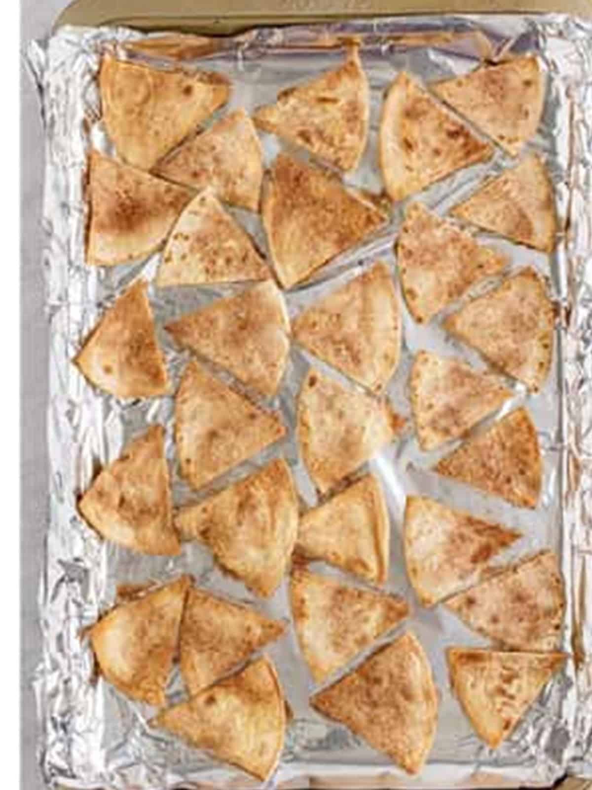 Cinnamon sugar tortilla chips baked golden brown on a foil lined sheet pan.