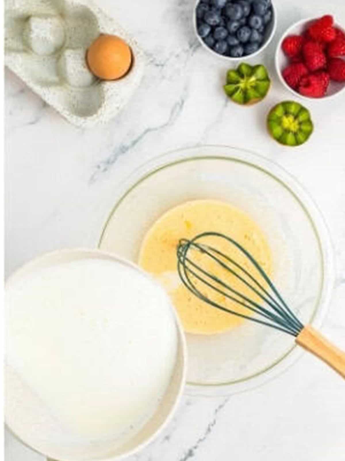 Drizzling hot milk into the egg mixture to temper it for fruit tartlet pastry cream.
