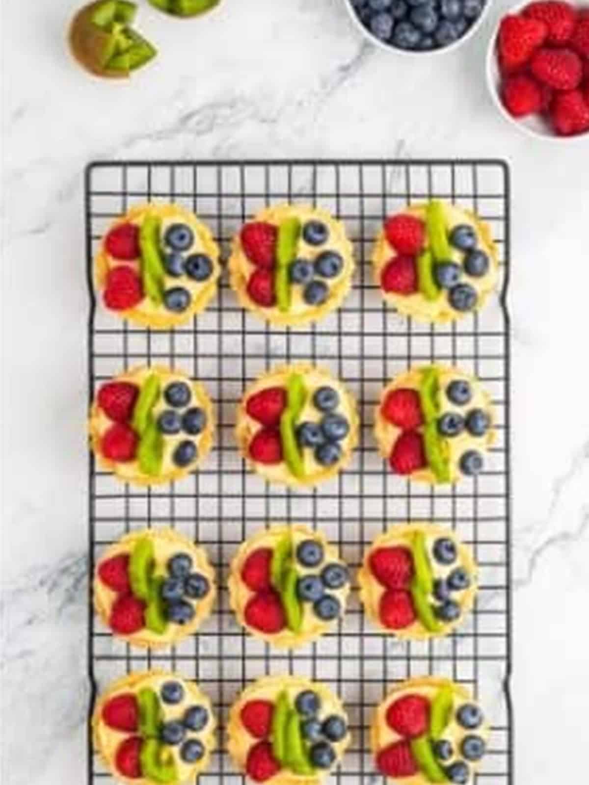 Mini fruit tartlets filled with pastry cream and topped with fresh blueberries, raspberries, and kiwi.