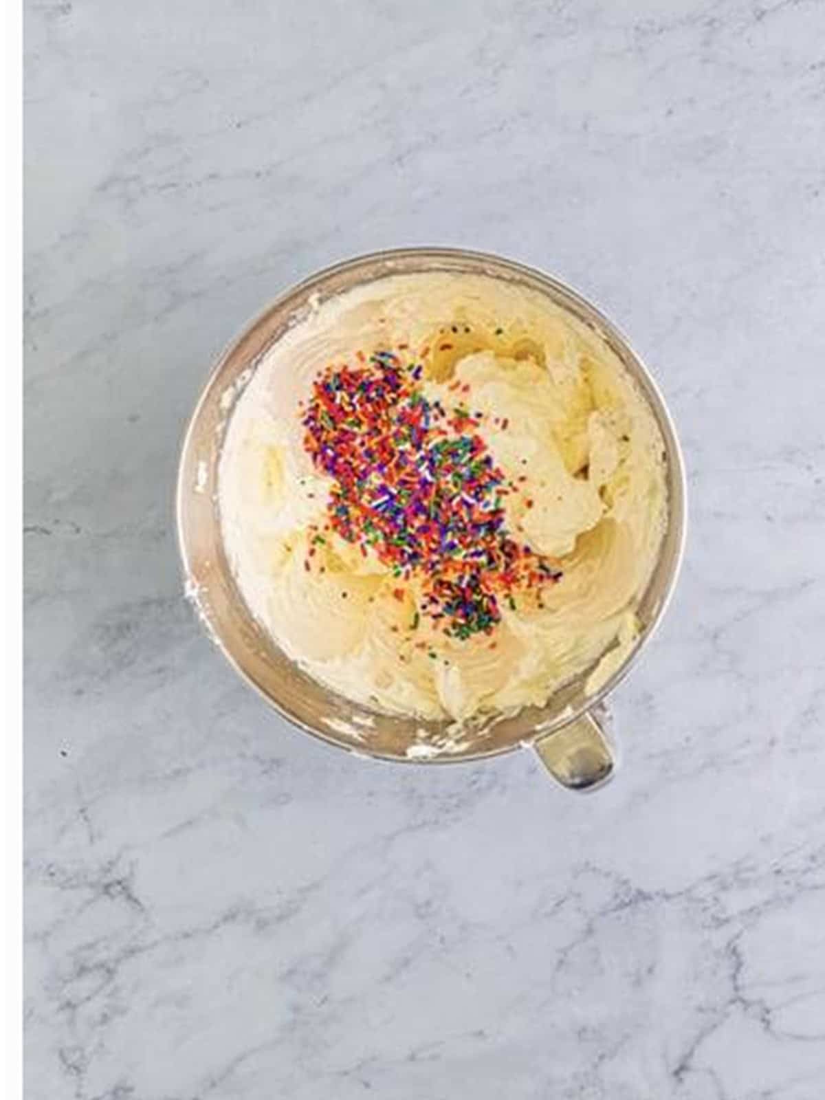 Stirring rainbow sprinkles into the vanilla frosting for Funfetti Cupcakes.