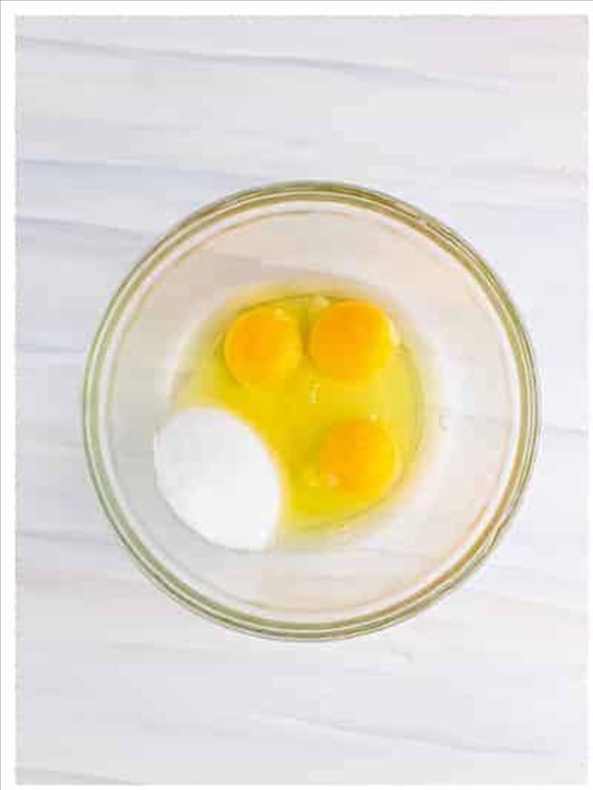 Eggs and sugar in a glass bowl for funnel cake recipe batter.